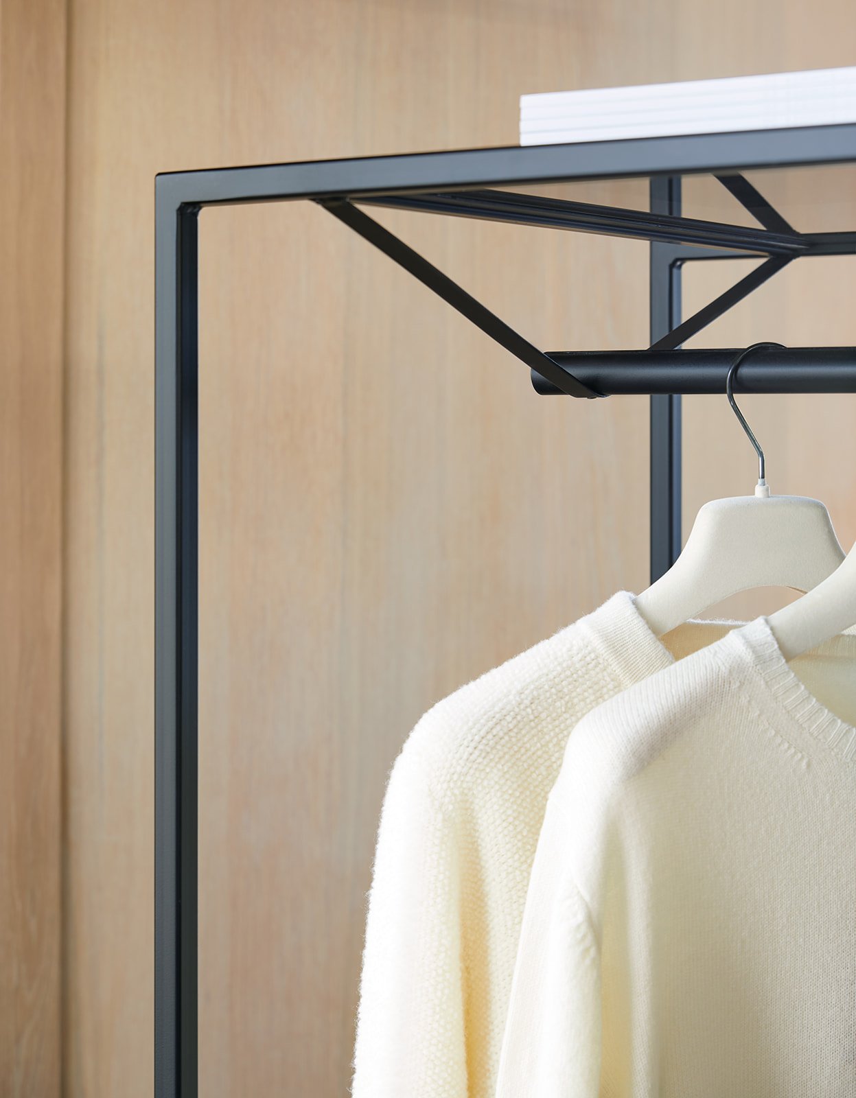 Cream-colored sweater hanging on a white hanger on a black clothing rack with a wooden wall background.