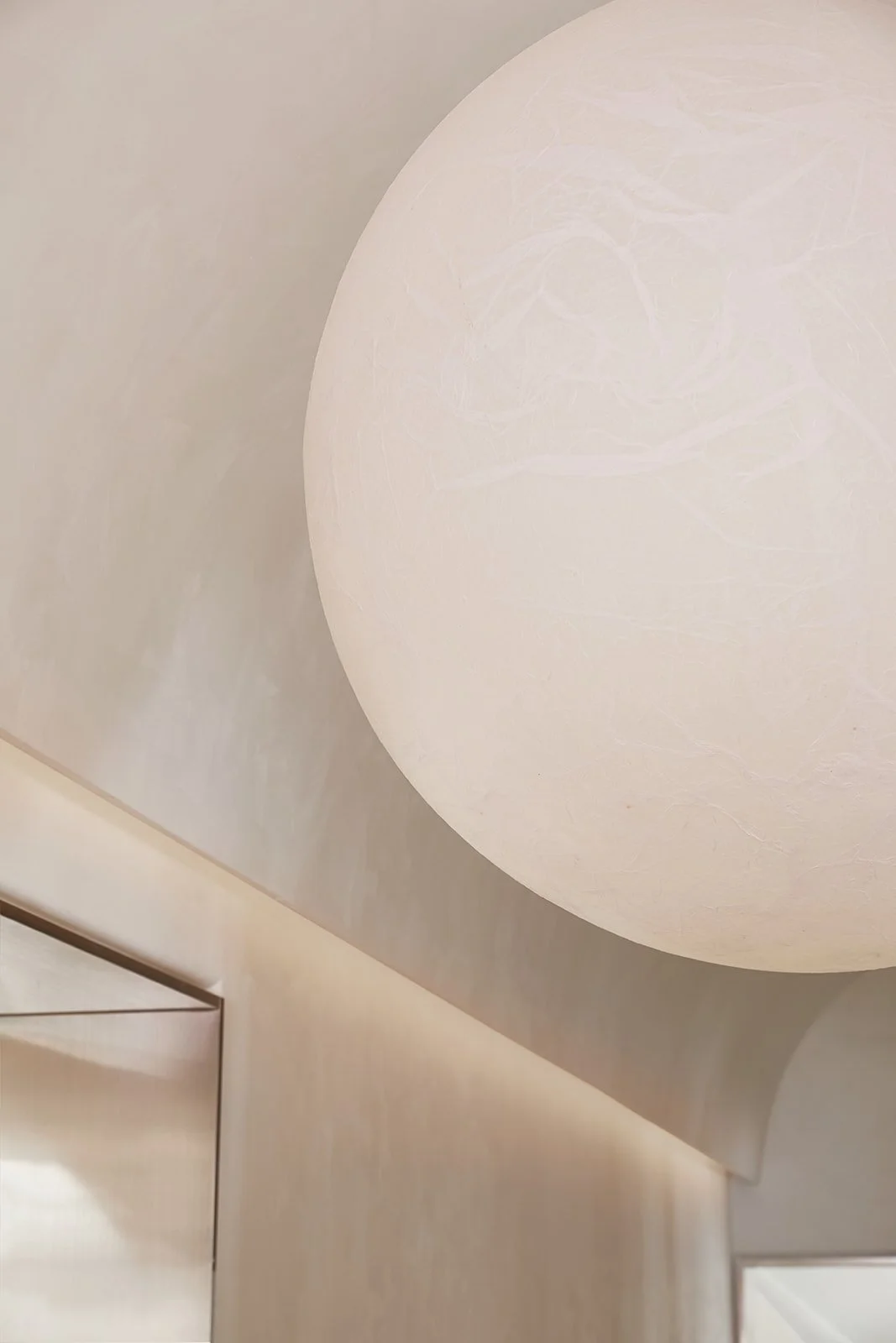 Close-up of a modern, minimalist ceiling light fixture with a spherical shape and soft white light in a neutral-colored room.