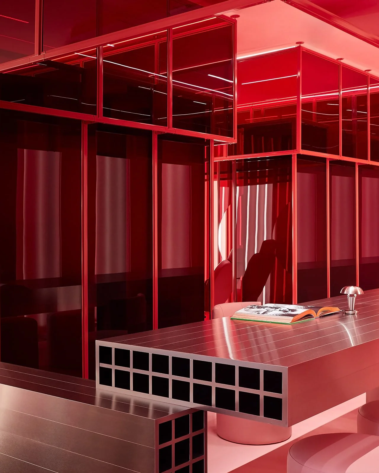 A dynamic interior shot of a luxury Toronto medical spa showcasing a bespoke cantilevered metal table, red glass room dividers, and an illuminated circular mirror that creates a surreal, restorative atmosphere.