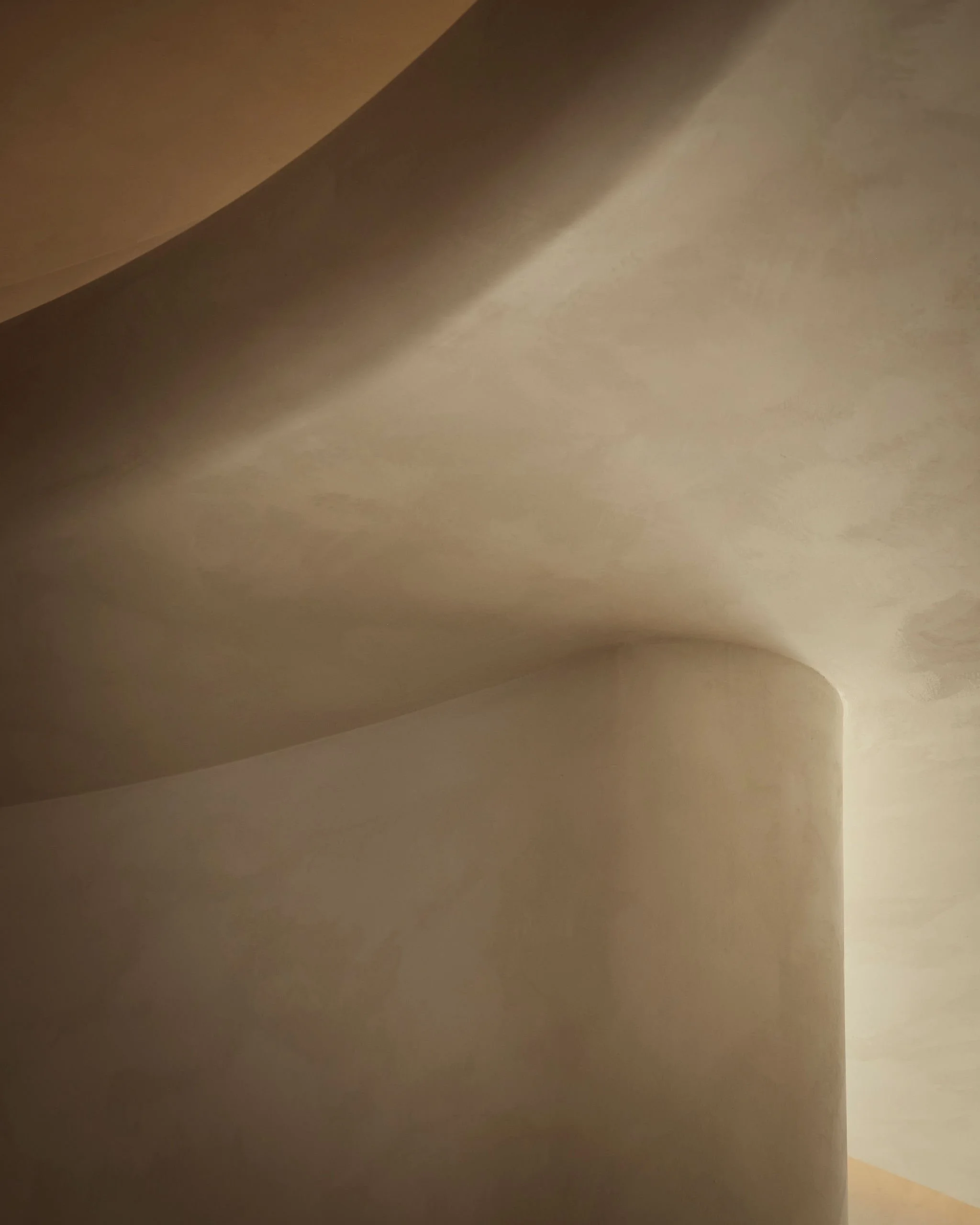 Abstract architectural detail of a curved limewash plaster wall and recessed ceiling illuminated by warm lighting in a modern minimalist wellness spa