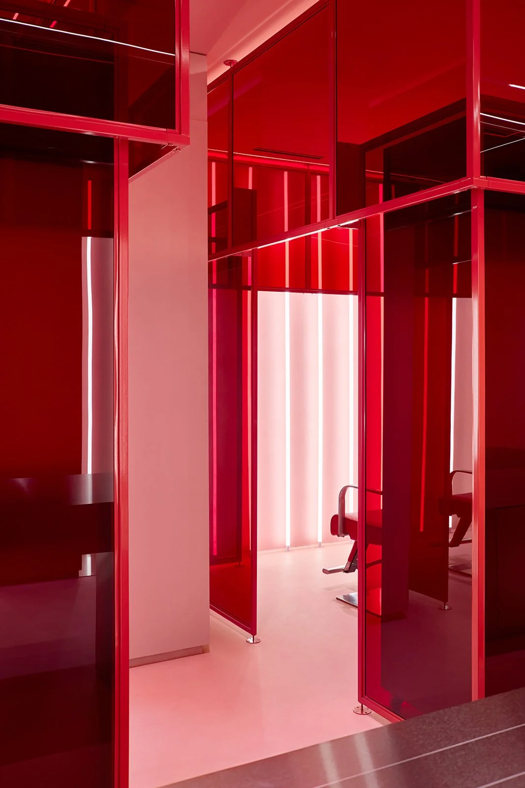 A vibrant corridor at Pout X medical spa framed by translucent red glass panels, leading into a private treatment room illuminated by continuous vertical ambient lighting.