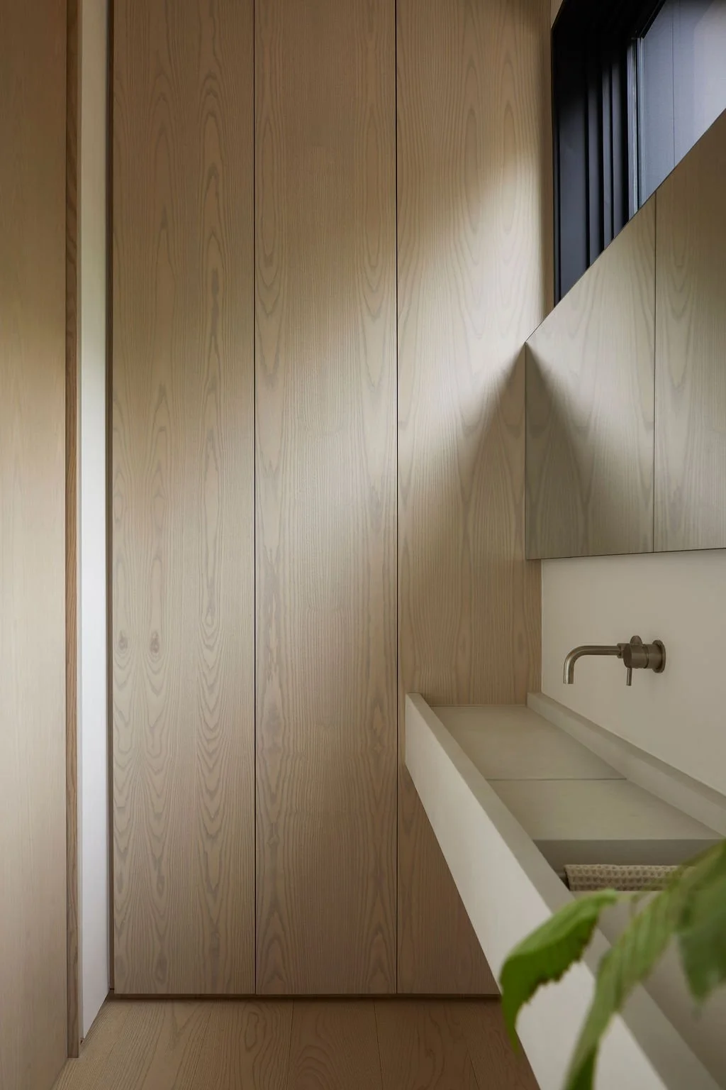 A minimalist bathroom in a private recreational residence featuring floor-to-ceiling light wood paneling, a custom concrete trough sink, and a modern wall-mounted faucet bathed in natural light.