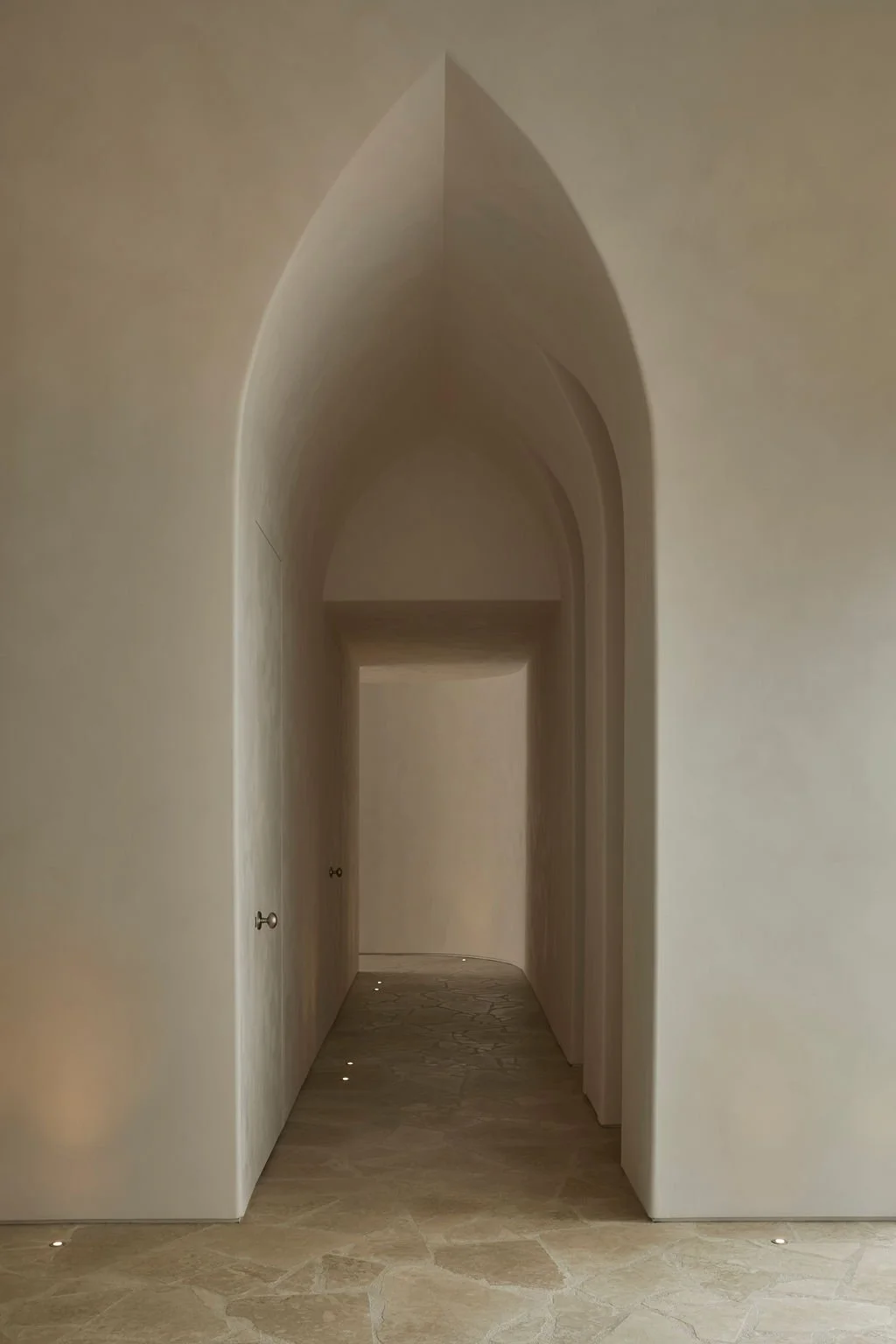 A serene corridor featuring a pointed architectural archway, textured limewash walls, and natural flagstone flooring at the Lune 1860 heritage property.