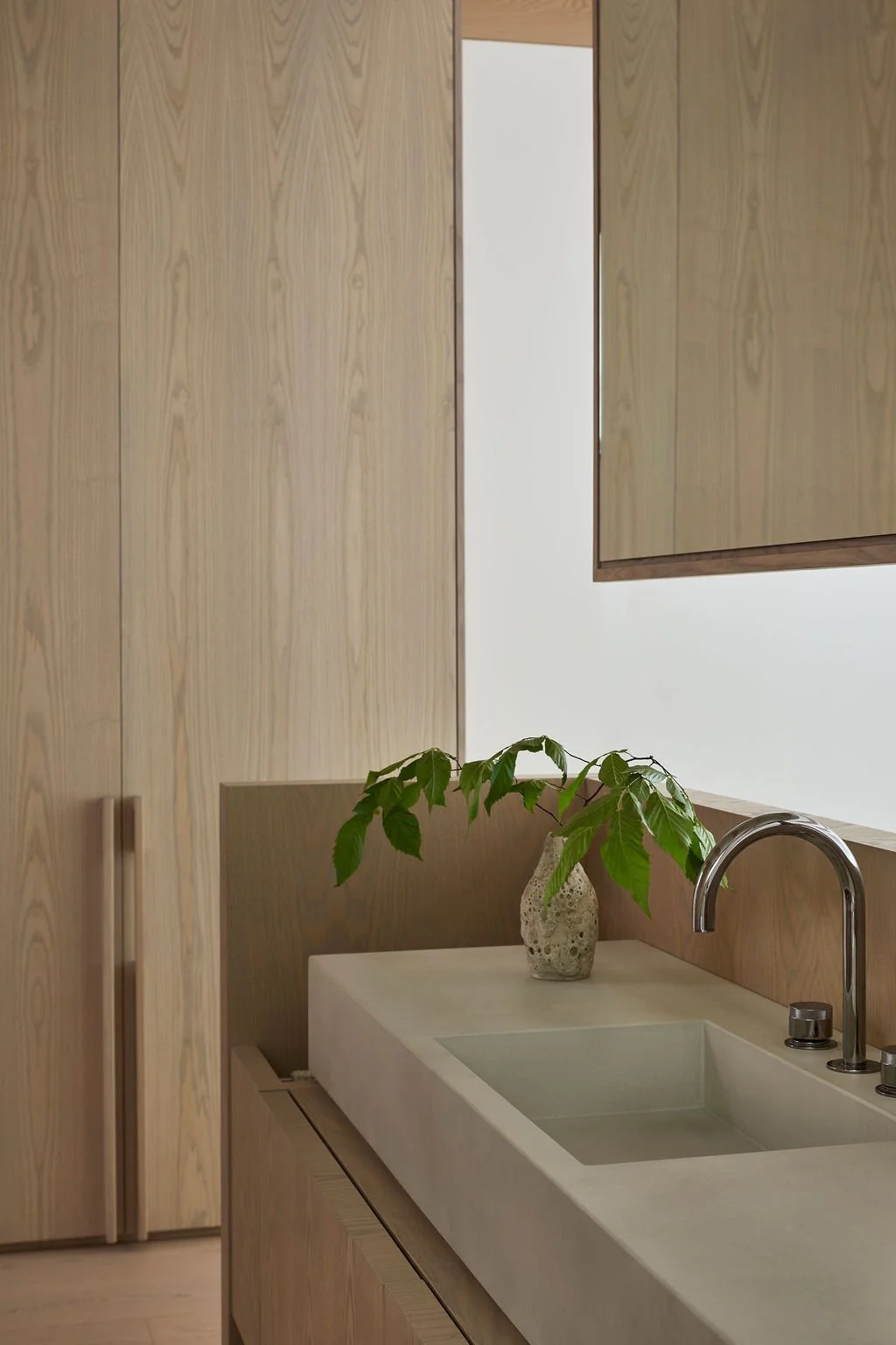 A bespoke bathroom vanity area in a recreational residence featuring a custom concrete sink basin integrated into light wood millwork, paired with a modern curved faucet and a wood-framed mirror.