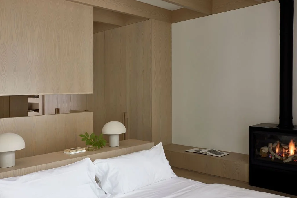 A cozy, minimalist bedroom in a private retreat featuring a low-profile bed, custom light wood architectural room dividers, and a modern freestanding fireplace.