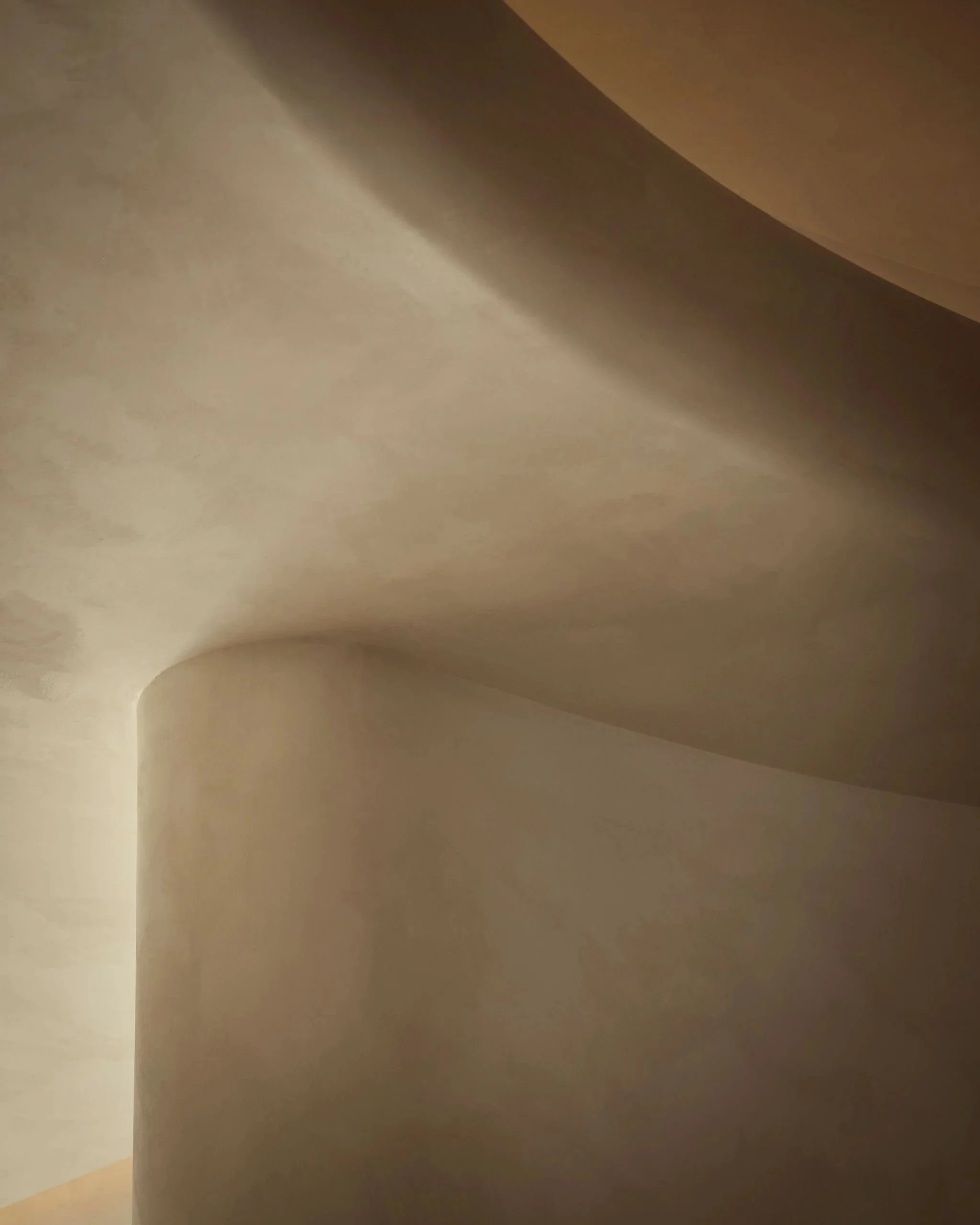 Abstract architectural detail of a curved limewash plaster wall and recessed ceiling illuminated by warm lighting in a modern minimalist wellness spa