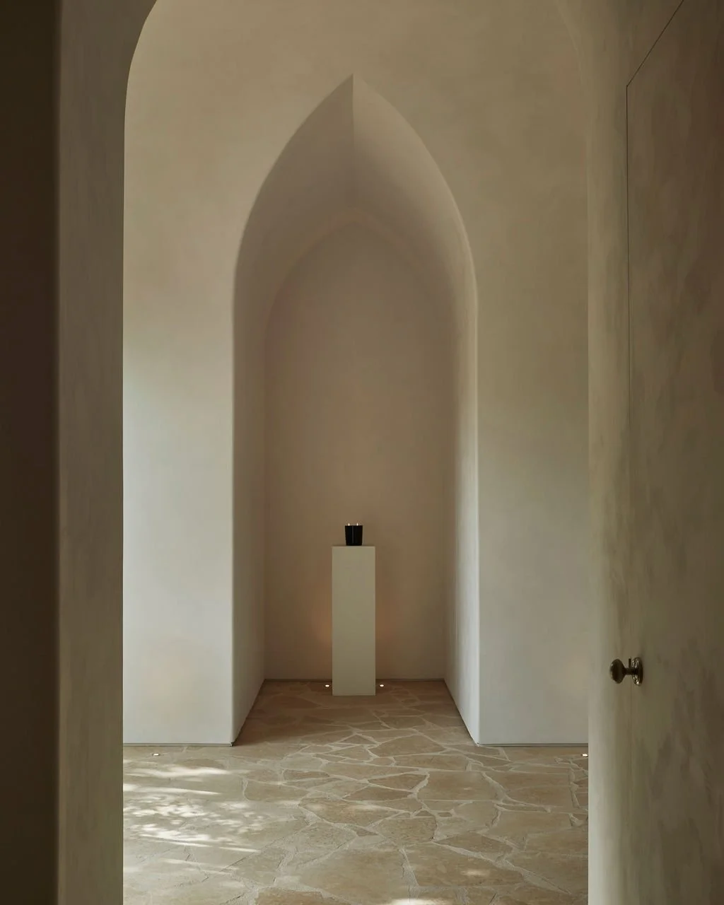A serene corridor featuring a pointed architectural archway, textured limewash walls, and natural flagstone flooring at the Lune 1860 heritage property.