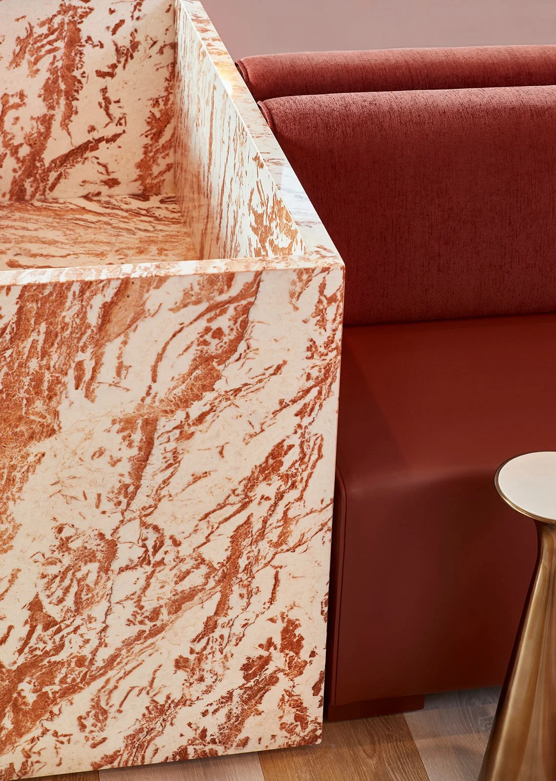 Close-up of a marble countertop with orange and white veining and a maroon upholstered booth with a small table beside it.