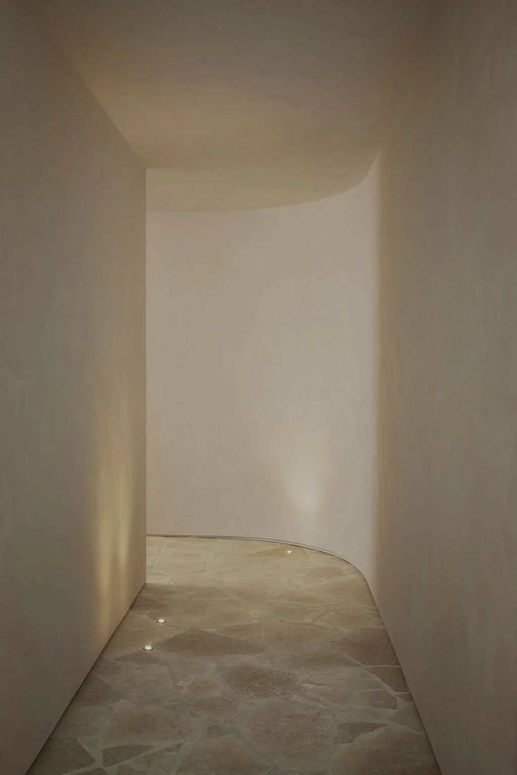 A serene corridor featuring a soft curving wall, textured limewash walls, and natural flagstone flooring at the Lune 1860 heritage property.