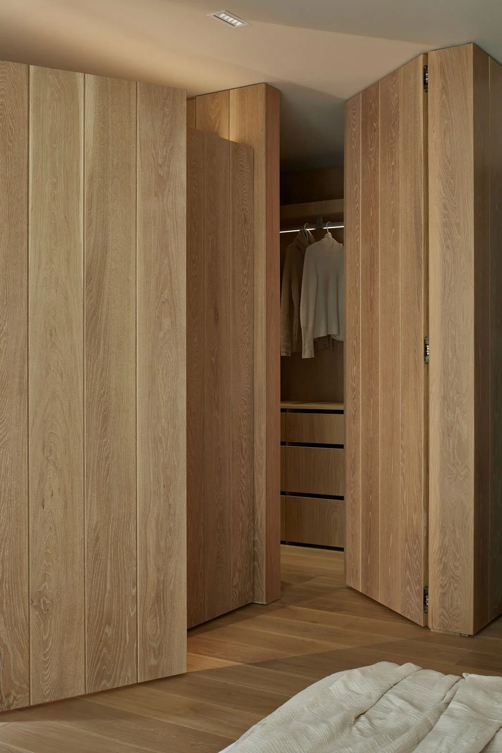 A seamless ribbed oak wood door stands open to reveal a bespoke walk-in closet, demonstrating elevated residential interior architecture and highly integrated hidden storage solutions.