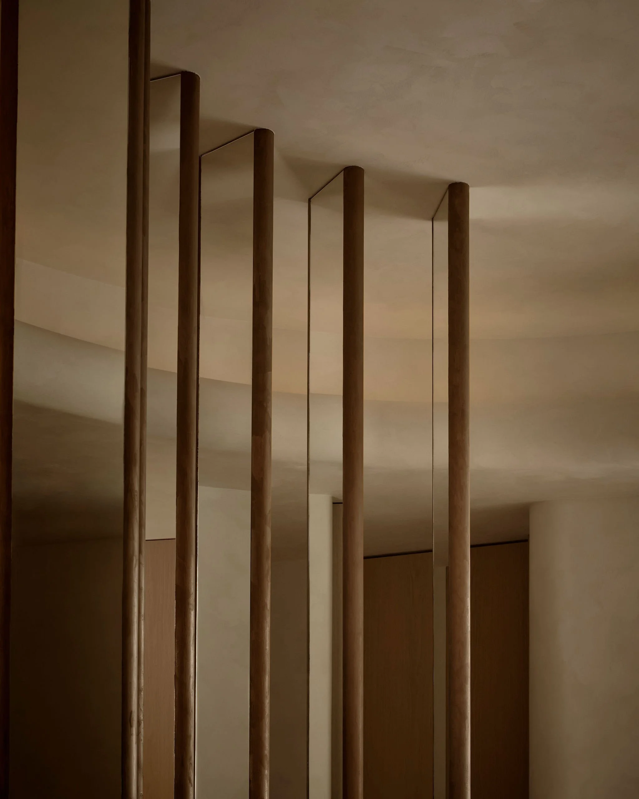 Close up architectural detail of a custom room divider made of vertical bronze plaster and mirrored panels, reaching up to a curved limewash plaster ceiling in a boutique plastic surgeons office