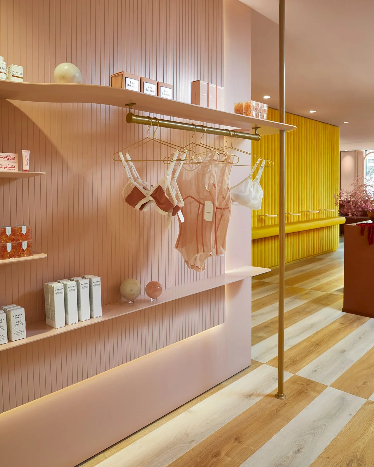 Display of women's lingerie and skincare products in a boutique store with pink and yellow decor.