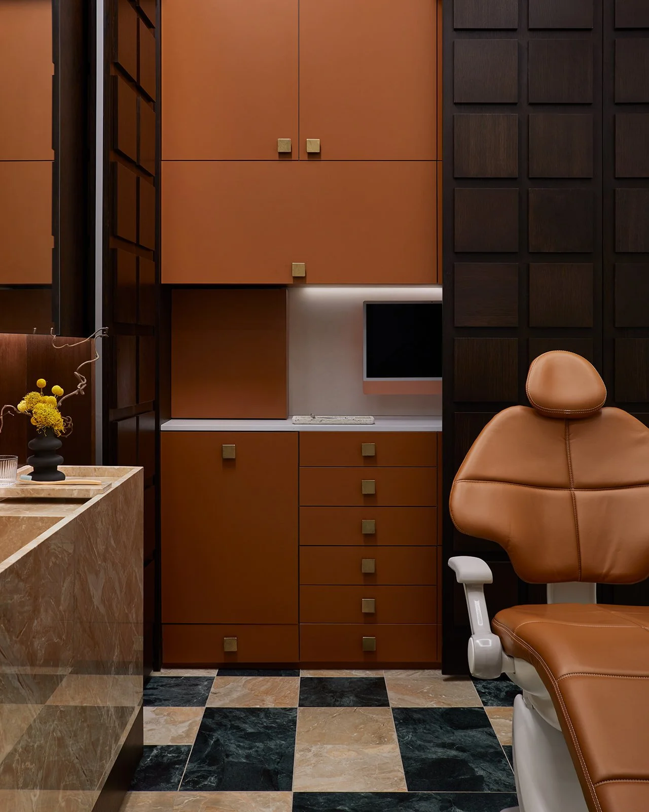 A demonstration of hidden architectural function in a dental operatory, showing dark wood grid panels opened to reveal highly organized, terracotta-colored clinical cabinetry and digital monitors.