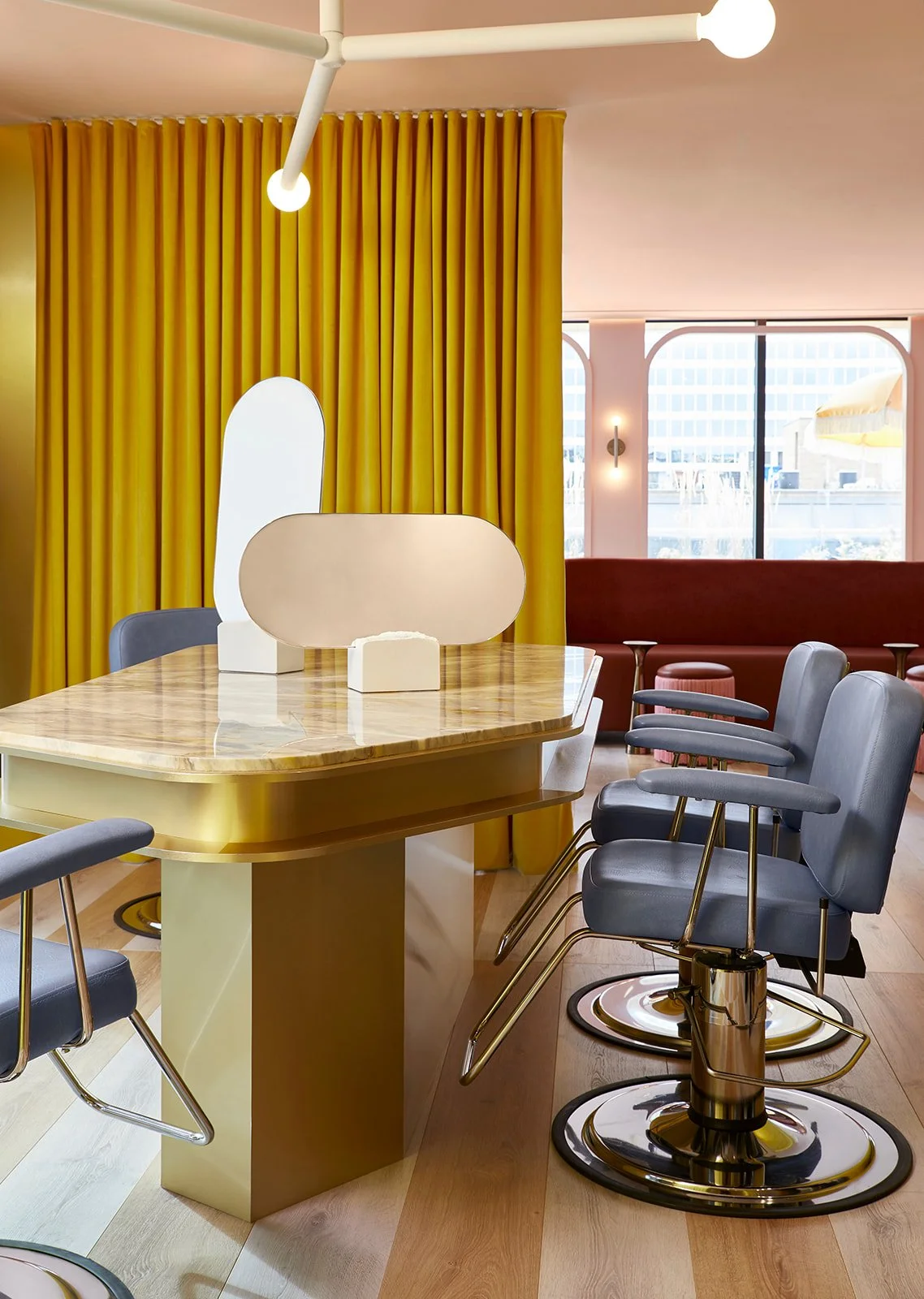 Interior of a modern dining area with a marble-topped table, blue chairs with gold accents, yellow curtains, and large windows letting in natural light.