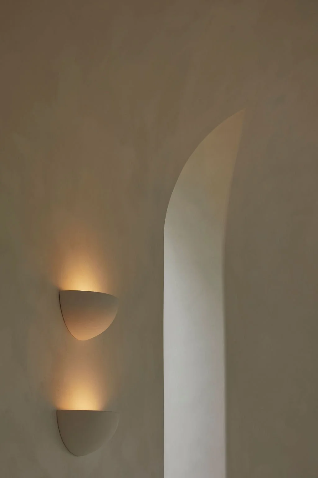 A close-up architectural detail of a curved, hand-troweled plaster window opening catching soft natural light in a bespoke hospitality interior.