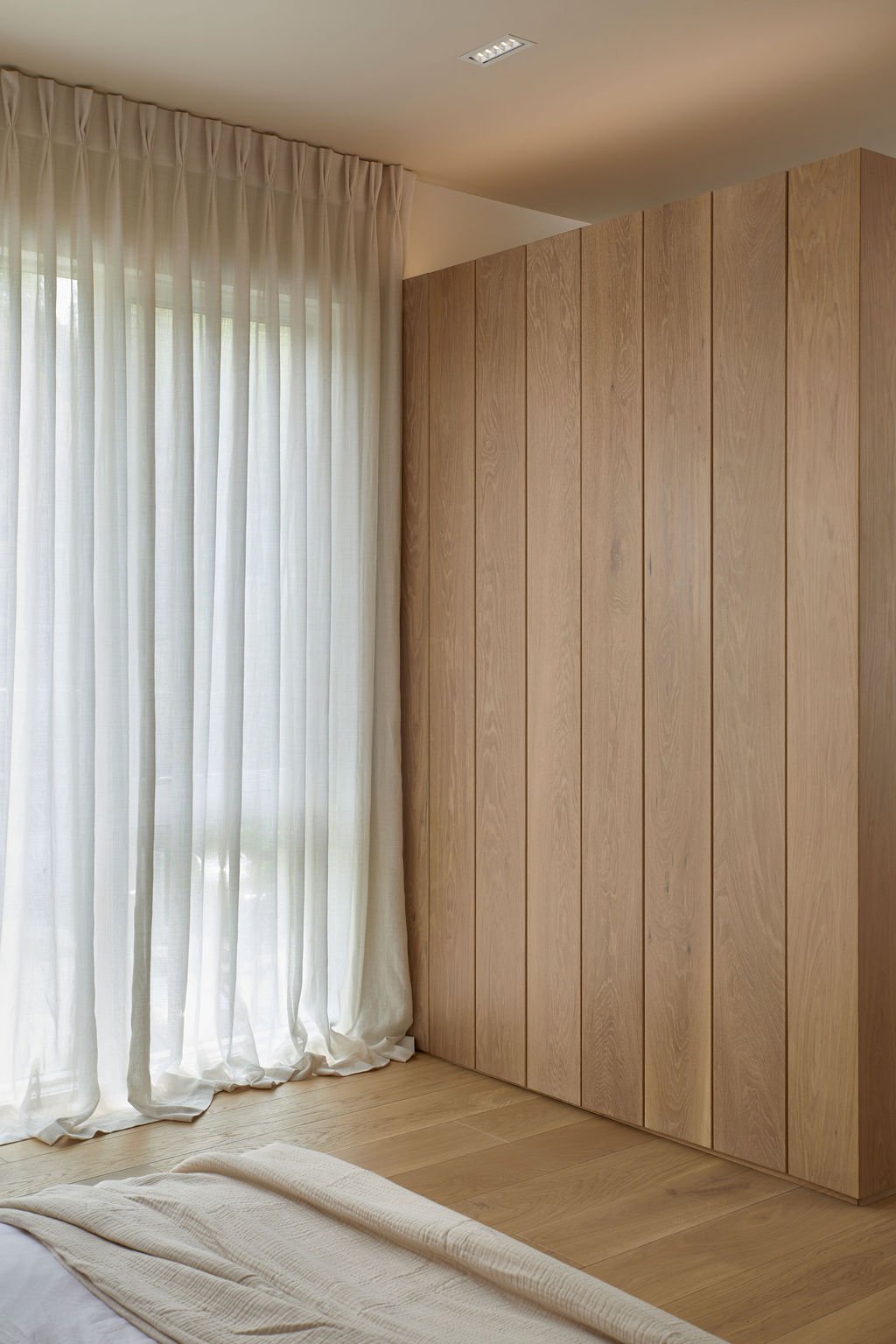 A detail shot highlighting the tactile material contrast between floor-to-ceiling bespoke ribbed oak wall paneling and soft, flowing sheer white window curtains in a high-end Toronto home.