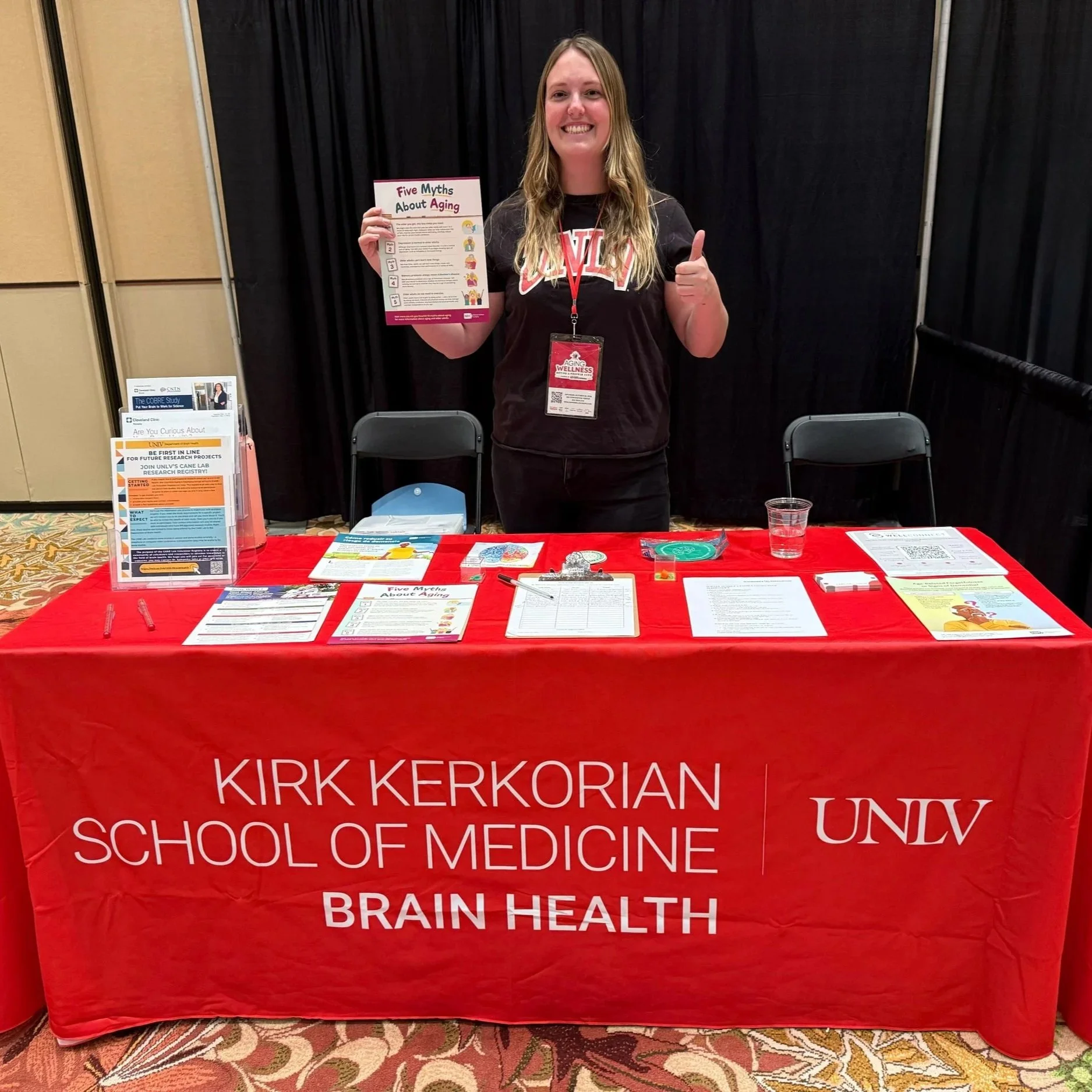 Grad Student Katie Singsank stand behind a table with resources giving a thumbs up