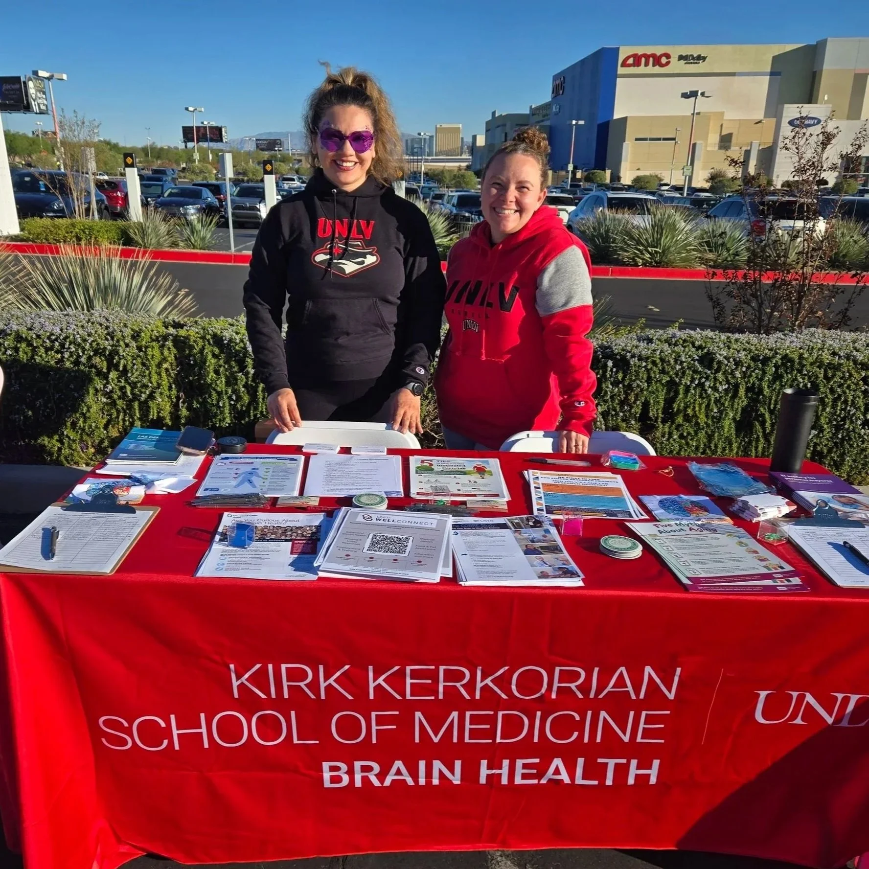 Cynthia Sopko and Kim Cobos stand behind a table with resources wearing UNLV gear