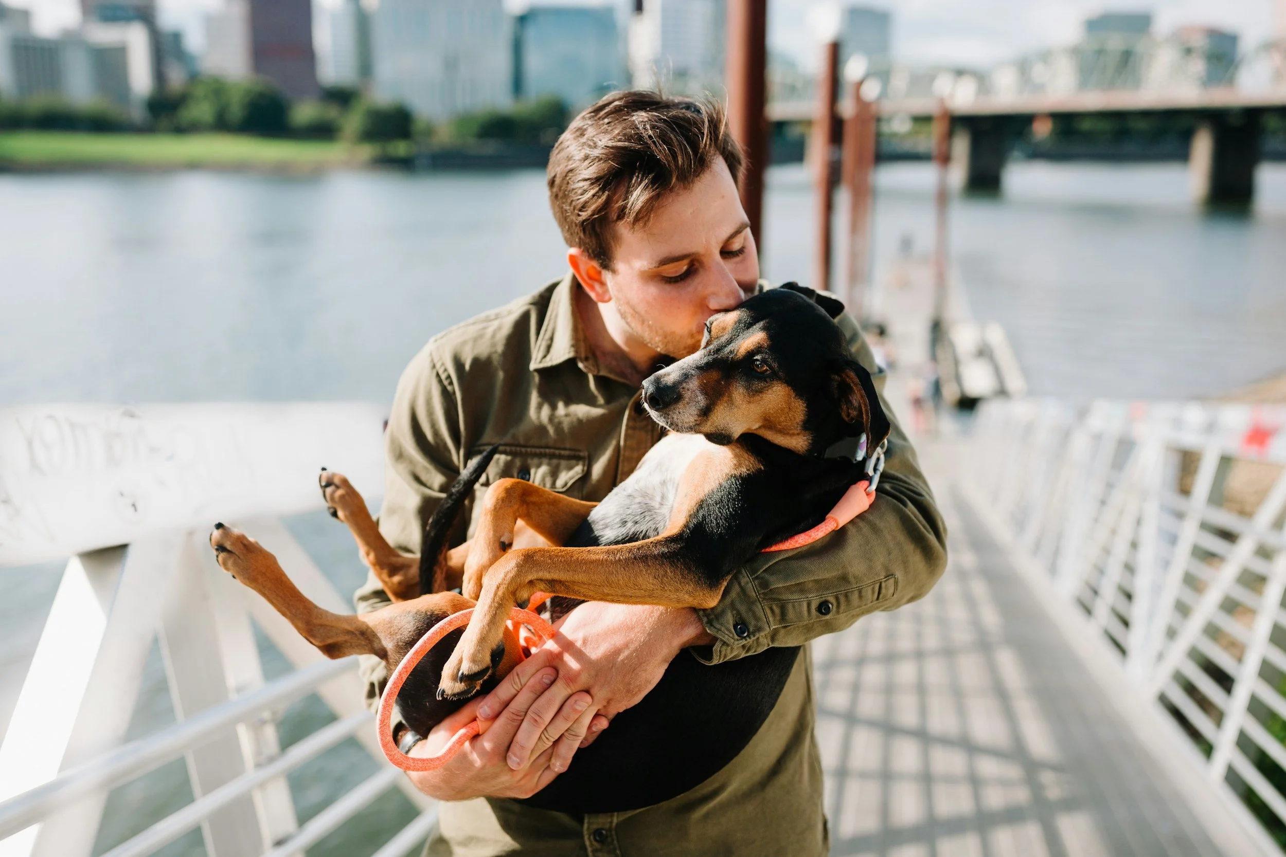 Man stands on a dock while holding his brown and black dog