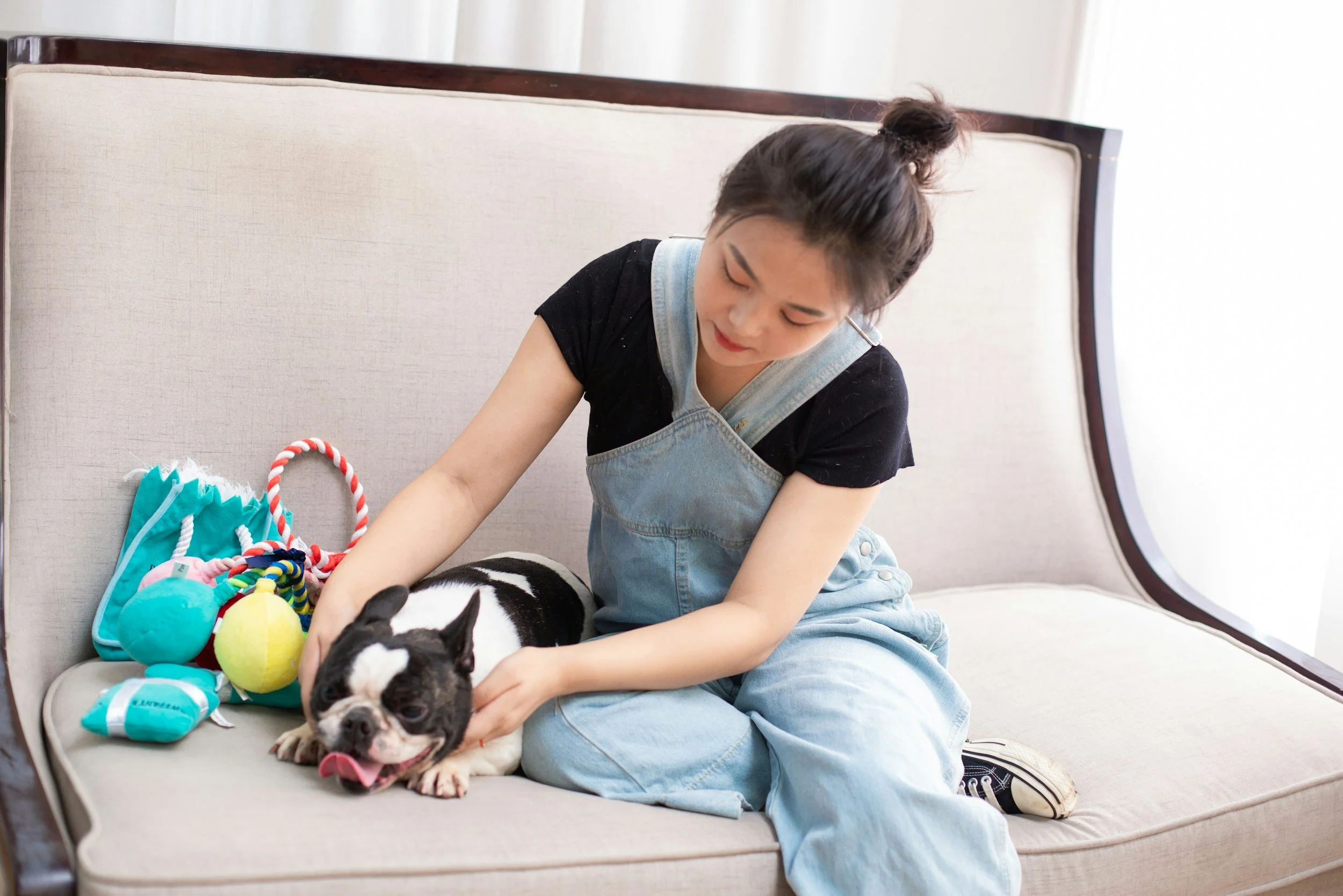 Woman sits on a couch and looks down at her black and white bulldog laying next to her