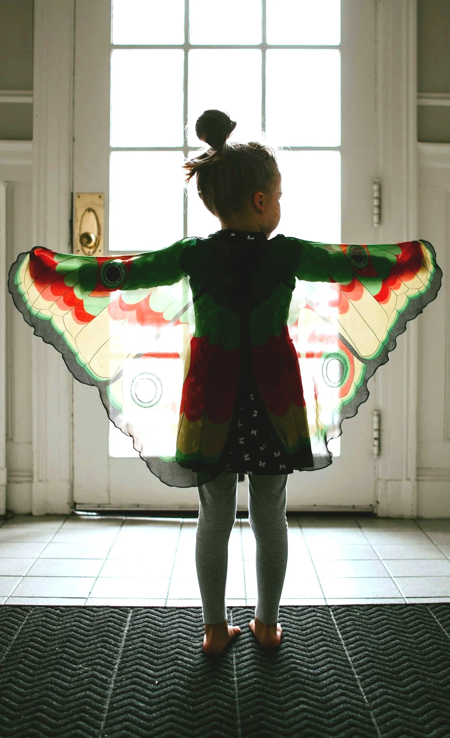 Young girl standing in front of a door spreads her arms, displaying butterfly wings