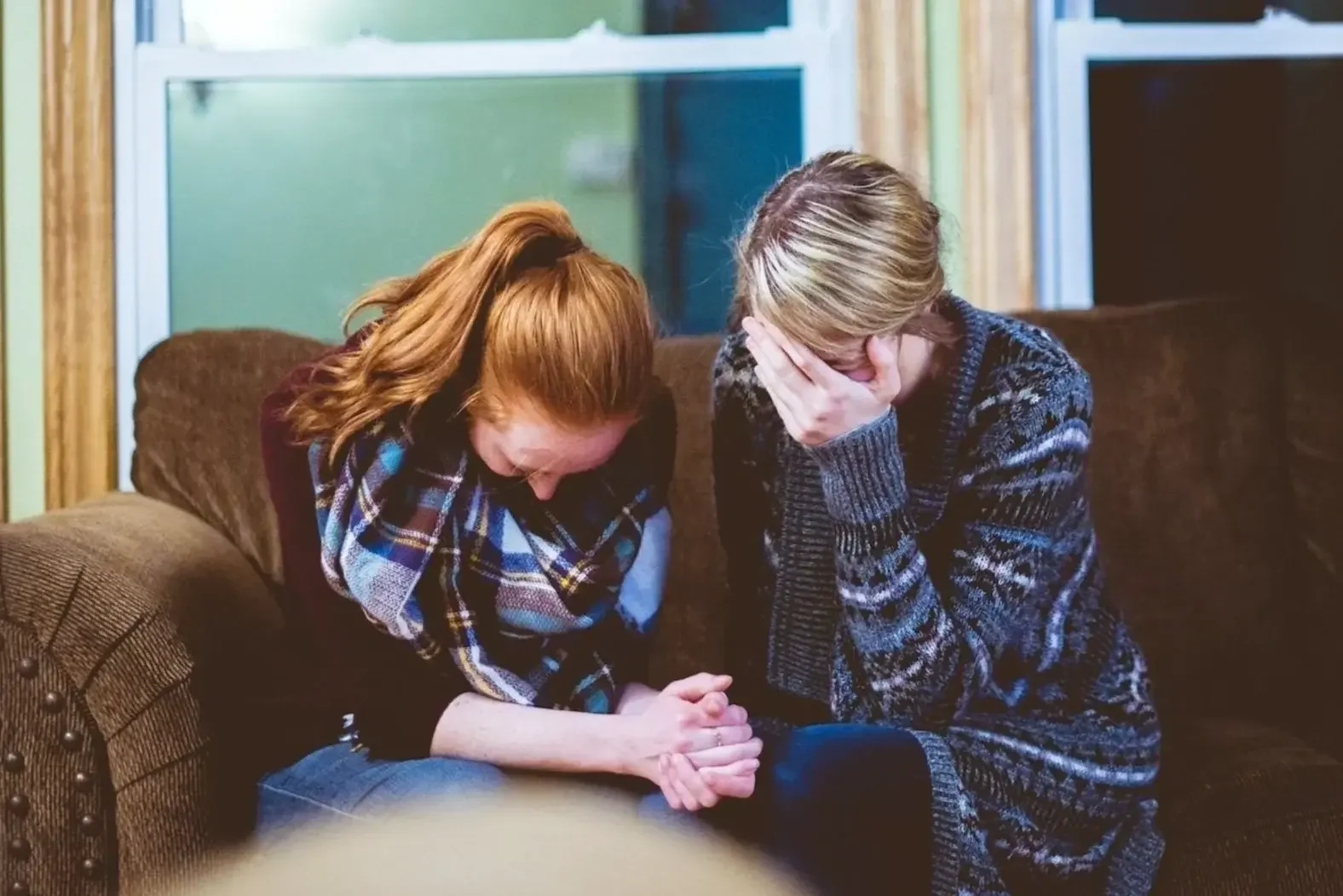 two women on couch looking down one with hand over her face