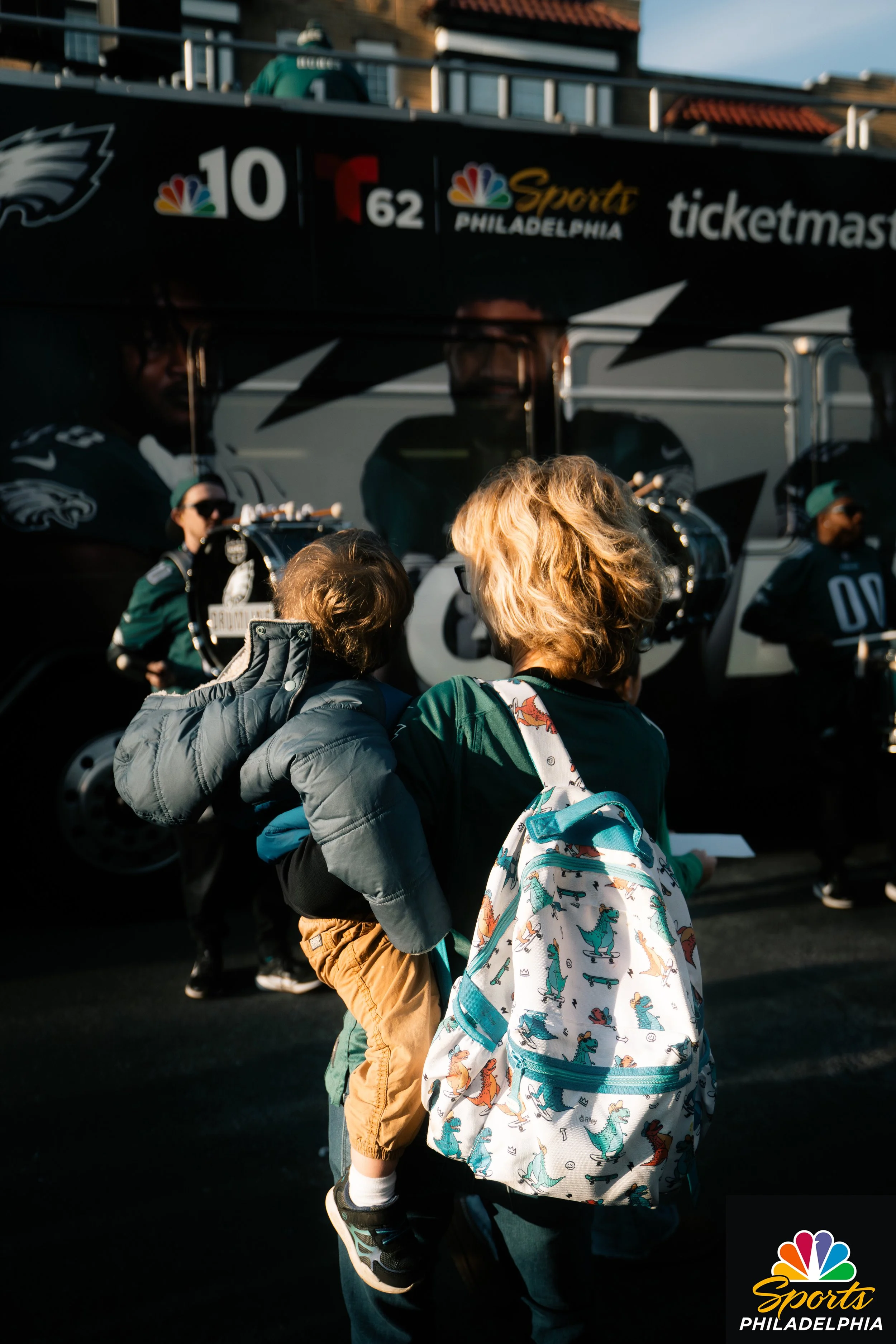 Children wearing backpacks waiting outside a sports stadium with NBC Sports Philadelphia and Ticketmaster signs.