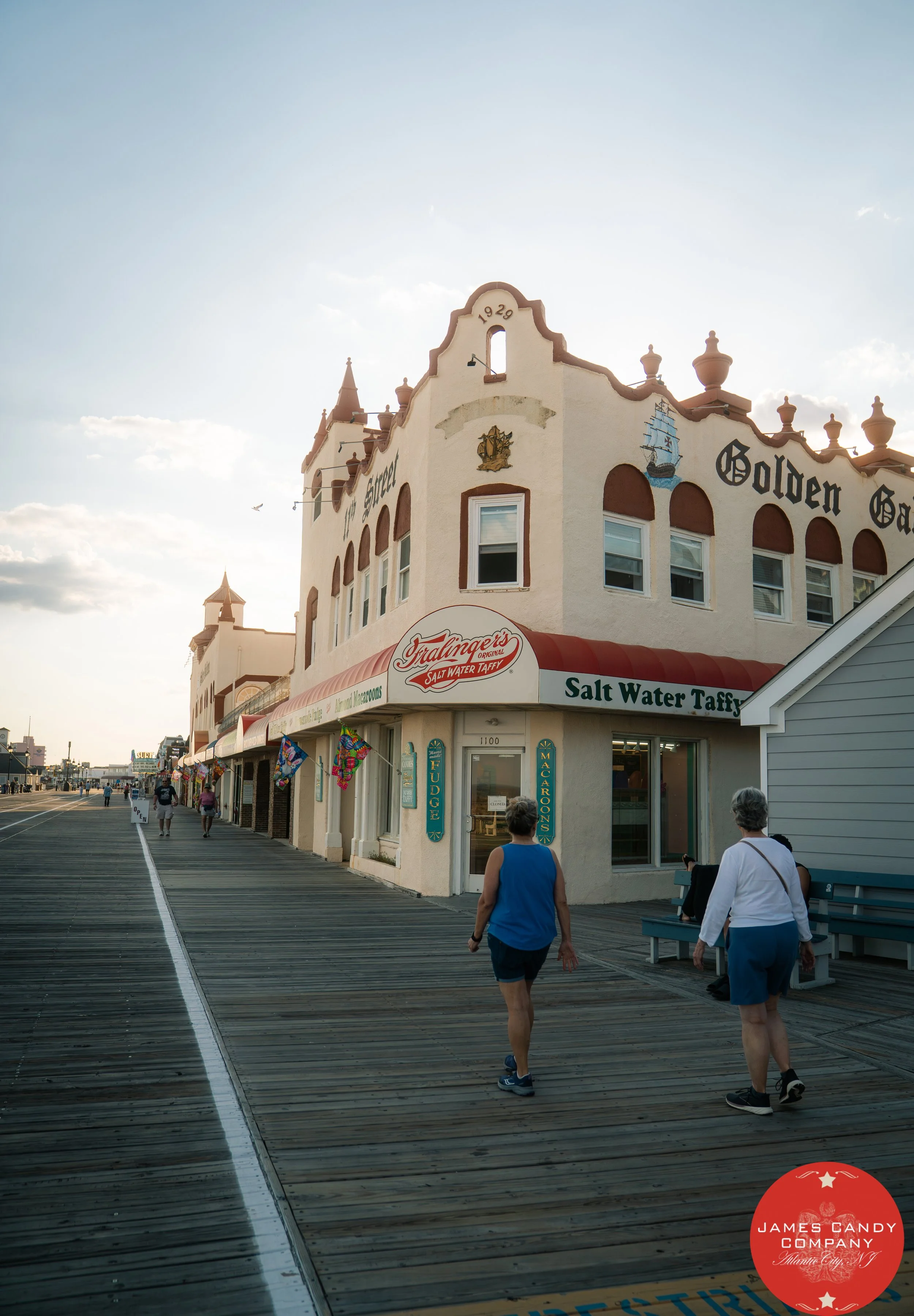 People walking on a wooden pier in Atlantic City, New Jersey, near shops and restaurants, with an old building decorated with maritime symbols and the words 'Golden Gate' on the facade.