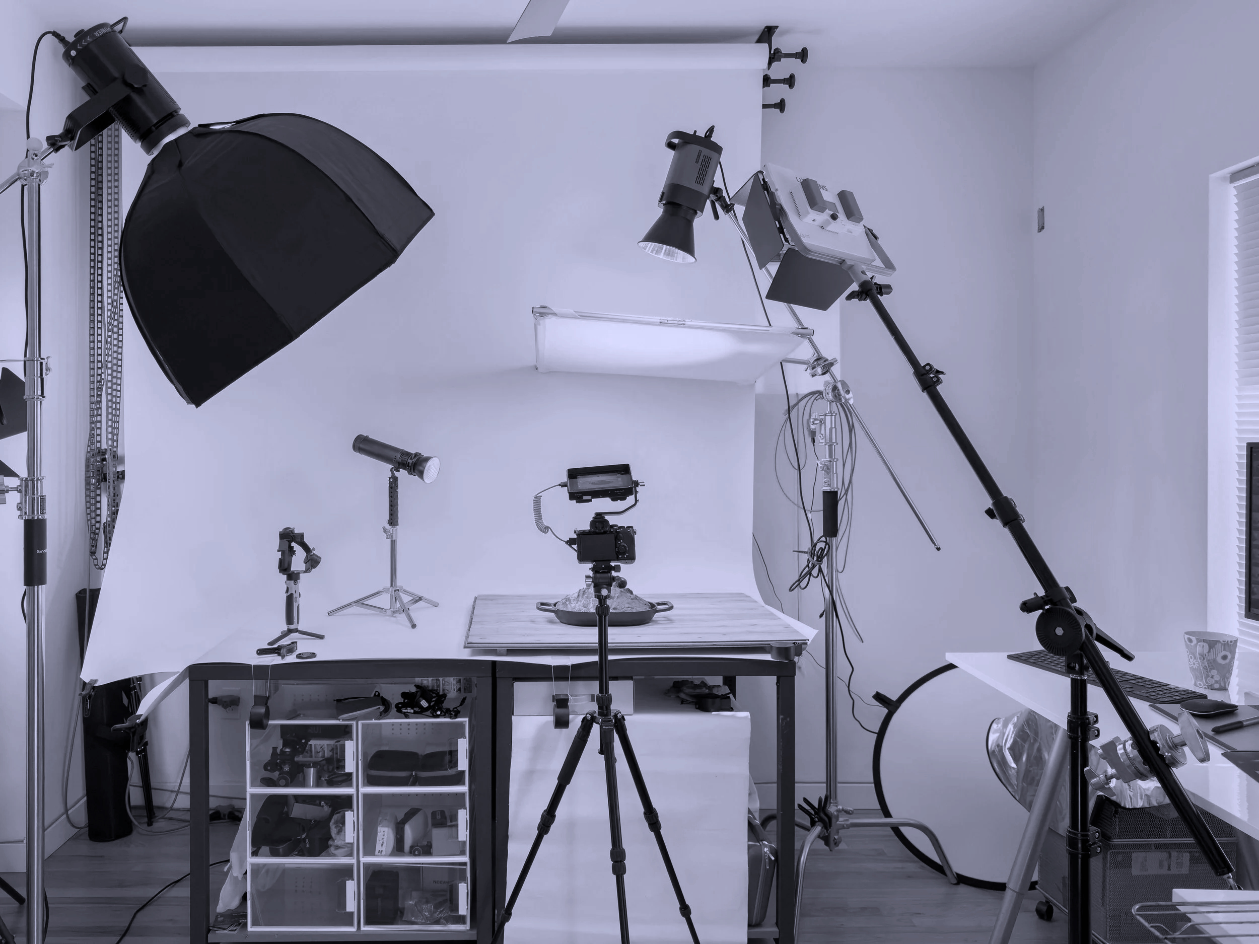 A photography studio setup with lighting and camera equipment, including softboxes, lights, and a backdrop on a white wall.