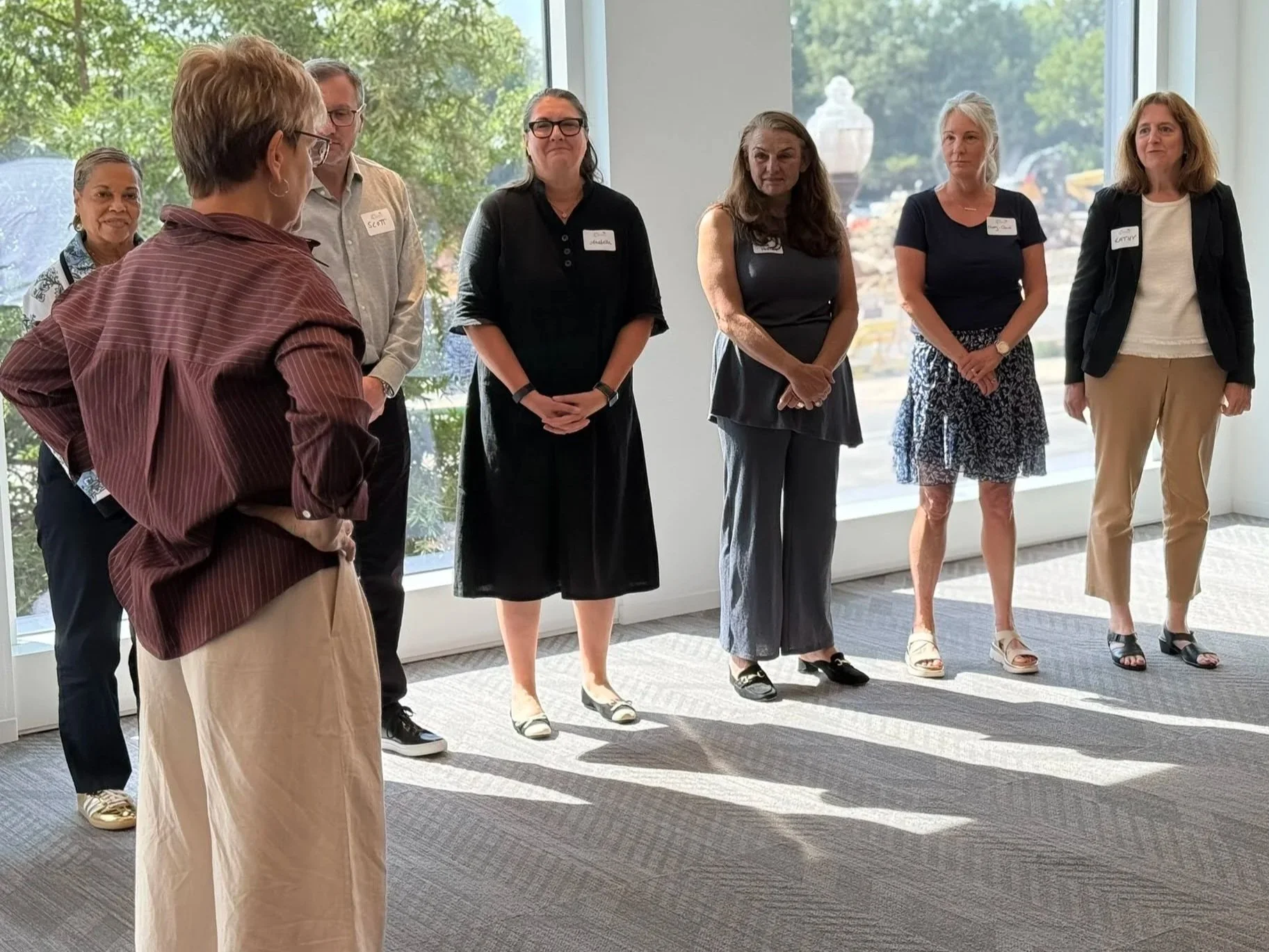 Group of adults standing indoors during a meeting in a bright room with large windows