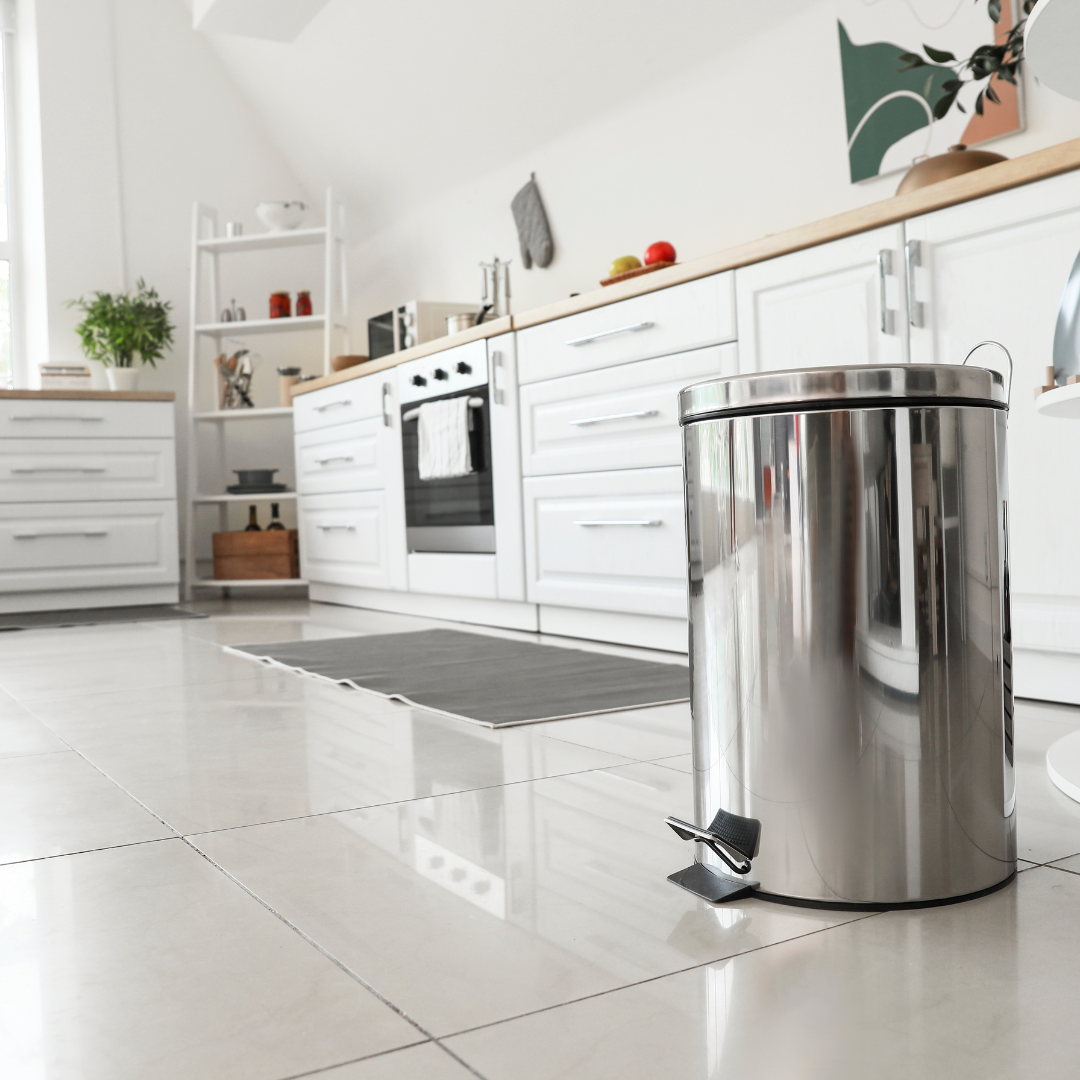 A minimal white kitchen with a stainless steel round trash can in the foreground.