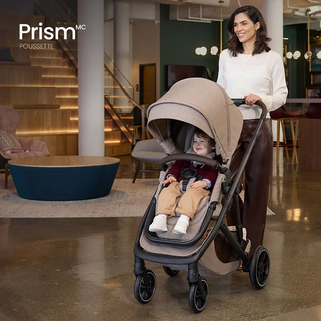 Poussette Prism. Une femme pousse un tout-petit dans une poussette dans un bâtiment moderne et élégant. 