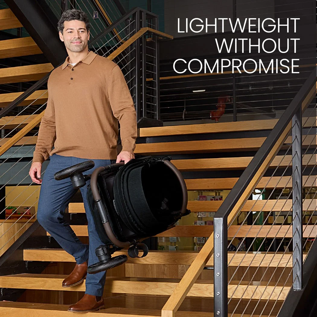 Lightweight without compromise. A man carrying a folded baby stroller down an indoor staircase.  