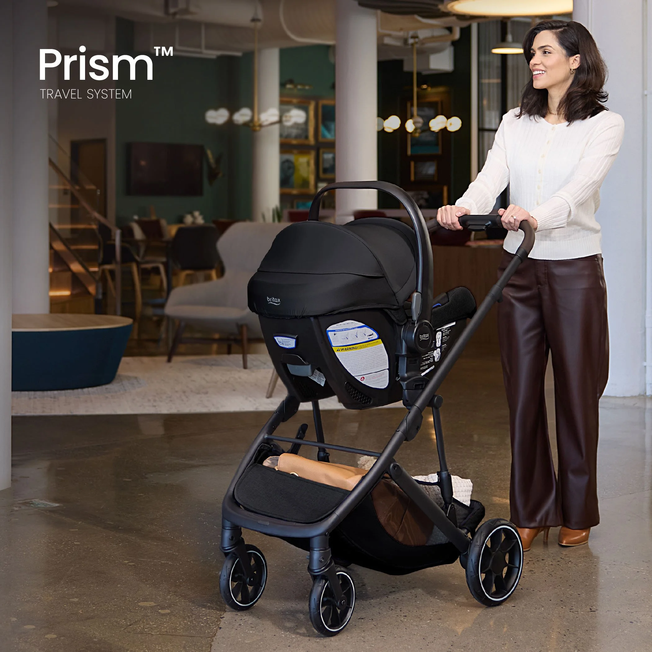 Prism travel system. A woman pushing a stroller with an infant car seat attached, inside of a building. 