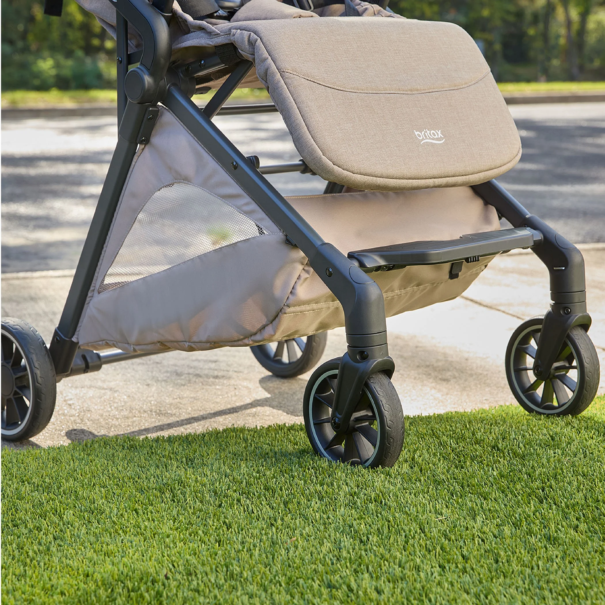 The bottom half of a stroller sitting outside between grass and the sidewalk.  