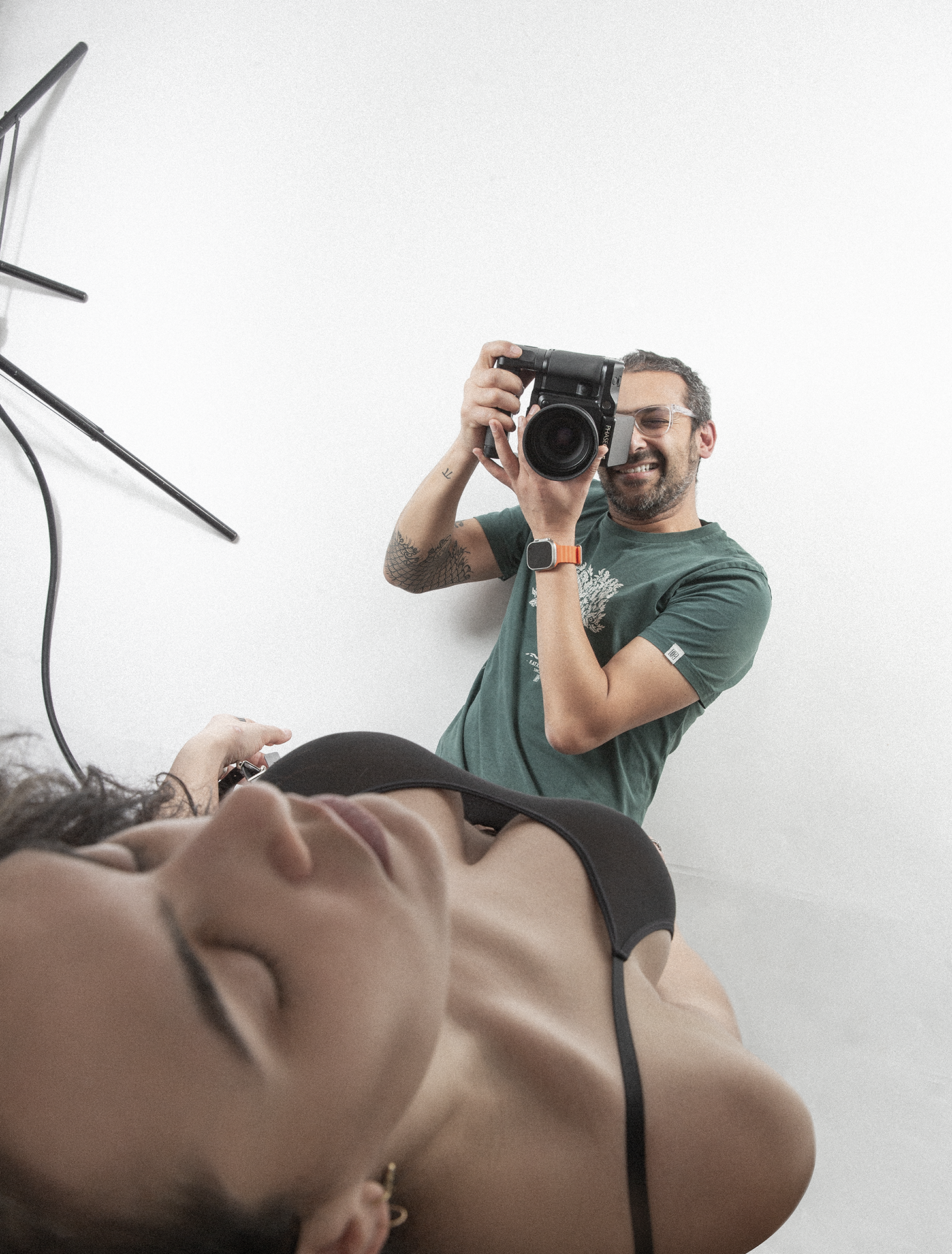 Autoportrait de Xavier Hennebel, prenant une photo d'une femme, allongé sur le sol dans son studio blanc.