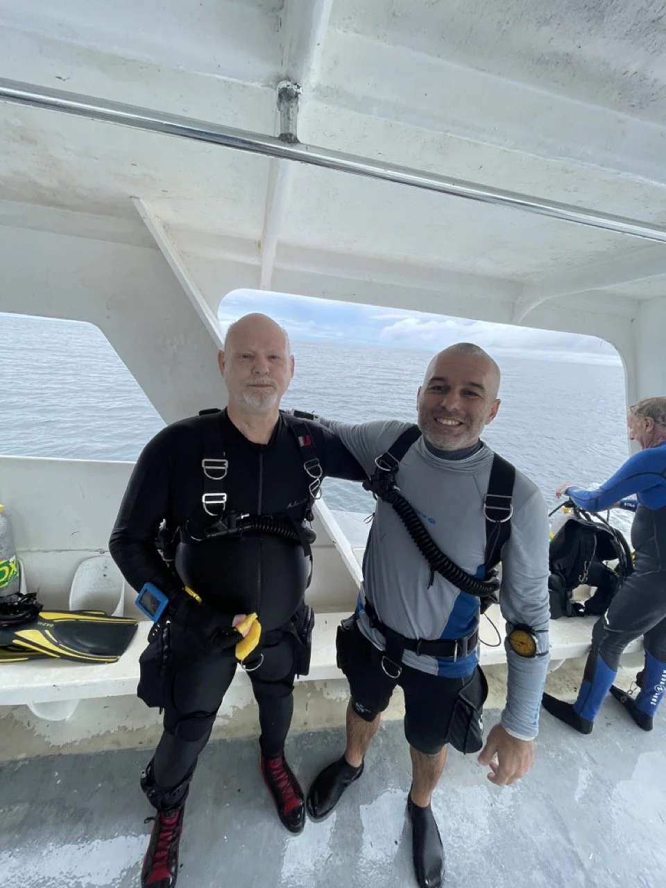 Two scuba divers wearing wetsuits and diving equipment standing on a boat with the ocean in the background.