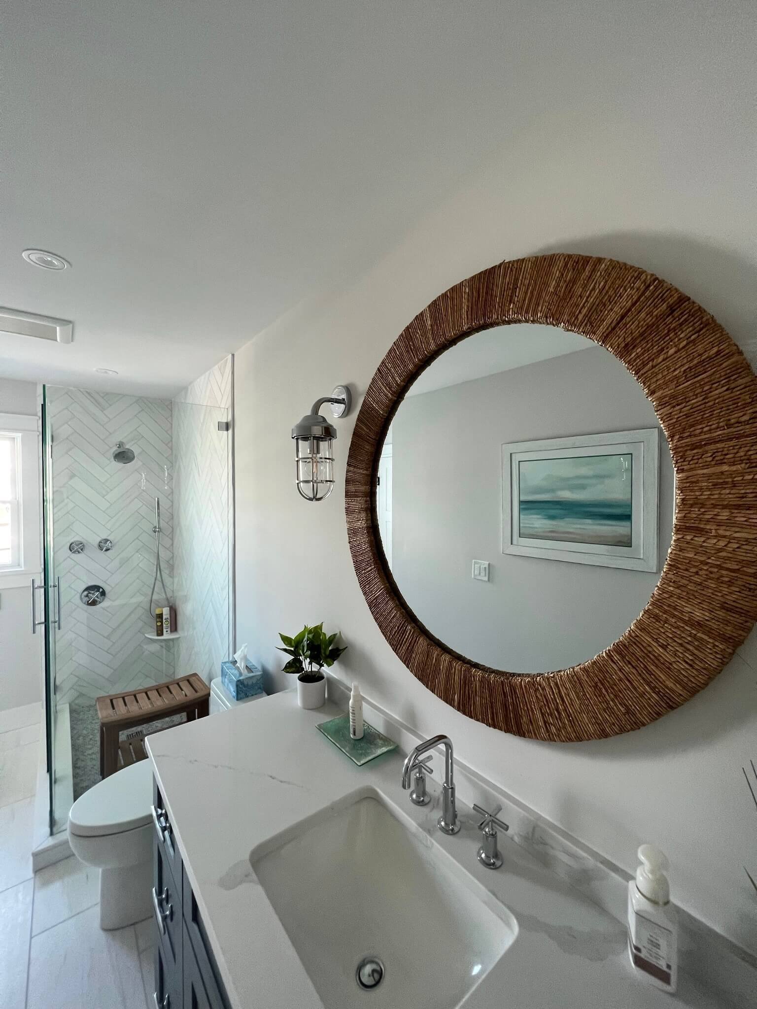 Coastal style bathroom with round woven mirror, quartz vanity, and herringbone shower tile in Ocean City, NJ