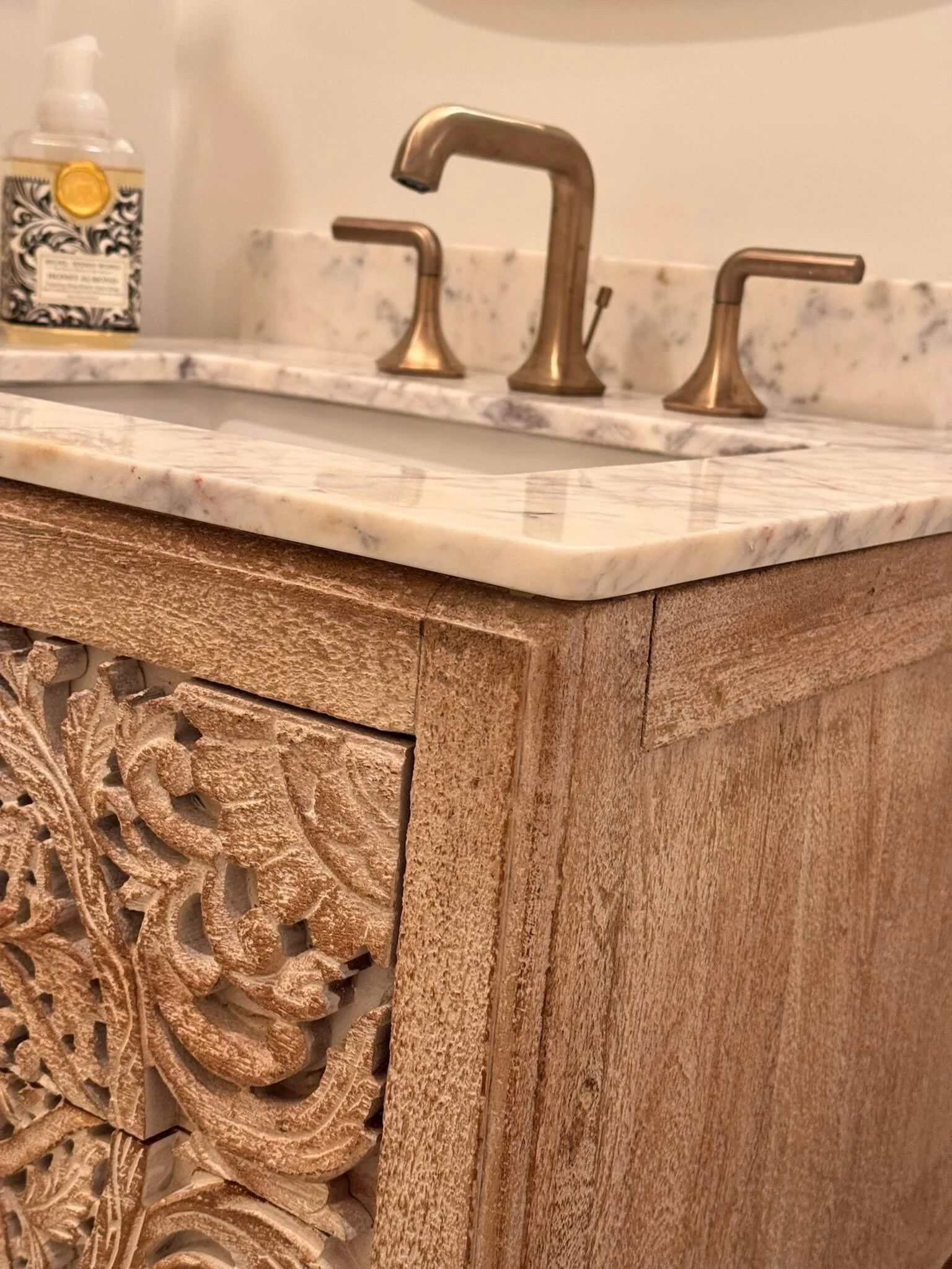 Hand-carved natural wood bathroom vanity with a polished marble countertop and brushed brass faucet, installed by 2B Contracting in Ocean City, NJ.