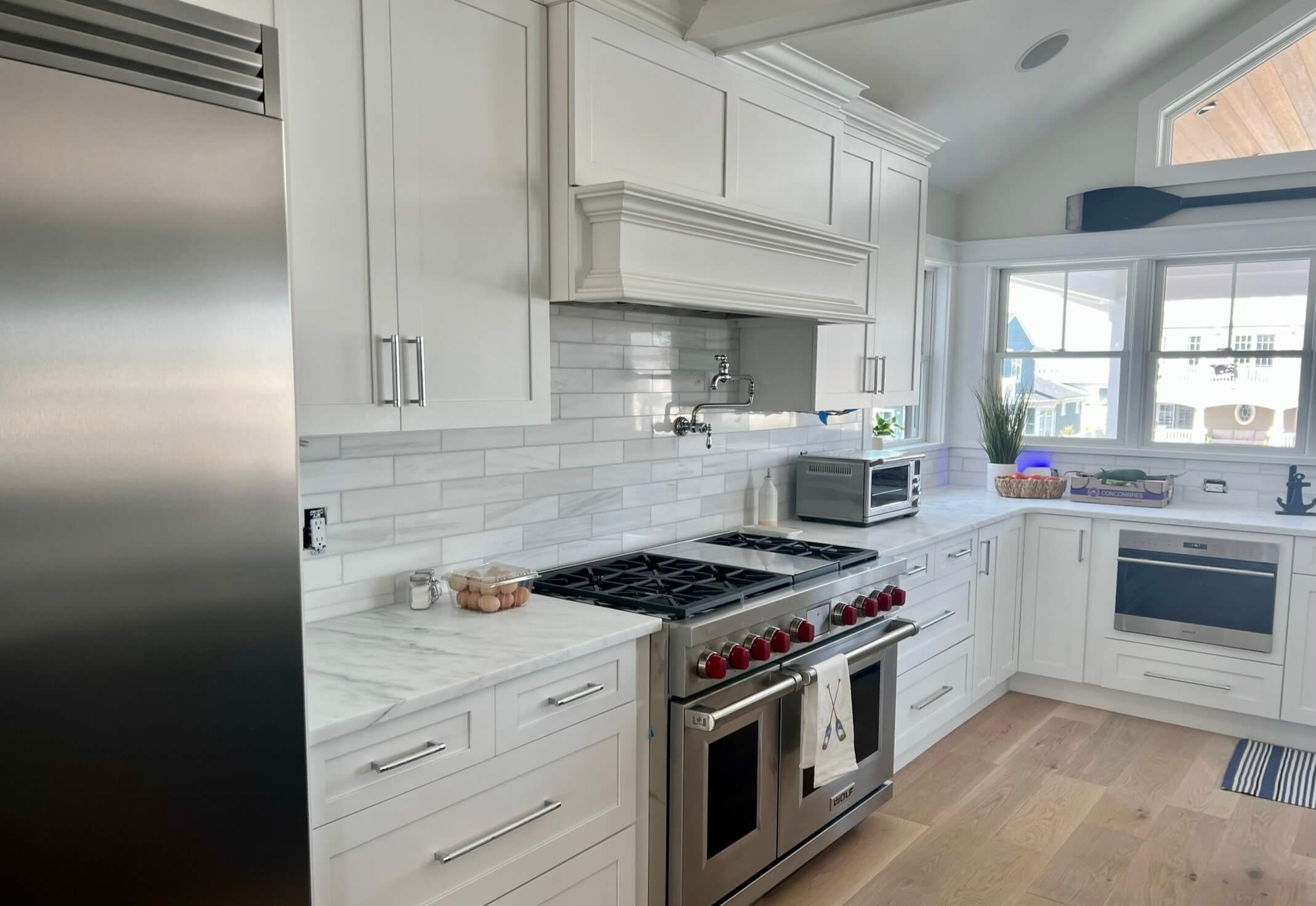 High-end kitchen renovation in Ocean City with a marble backsplash, custom range hood, premium gas stove, and shaker cabinetry by 2B Contracting.
