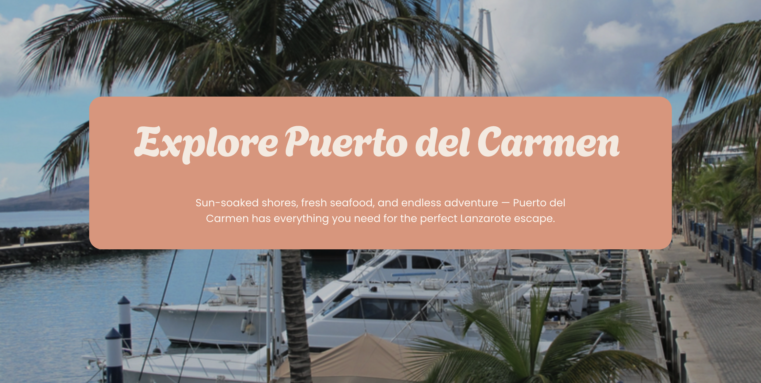 View of a marina in Puerto del Carmen with boats docked, surrounded by palm trees, with a hillside in the background, under a partly cloudy sky.