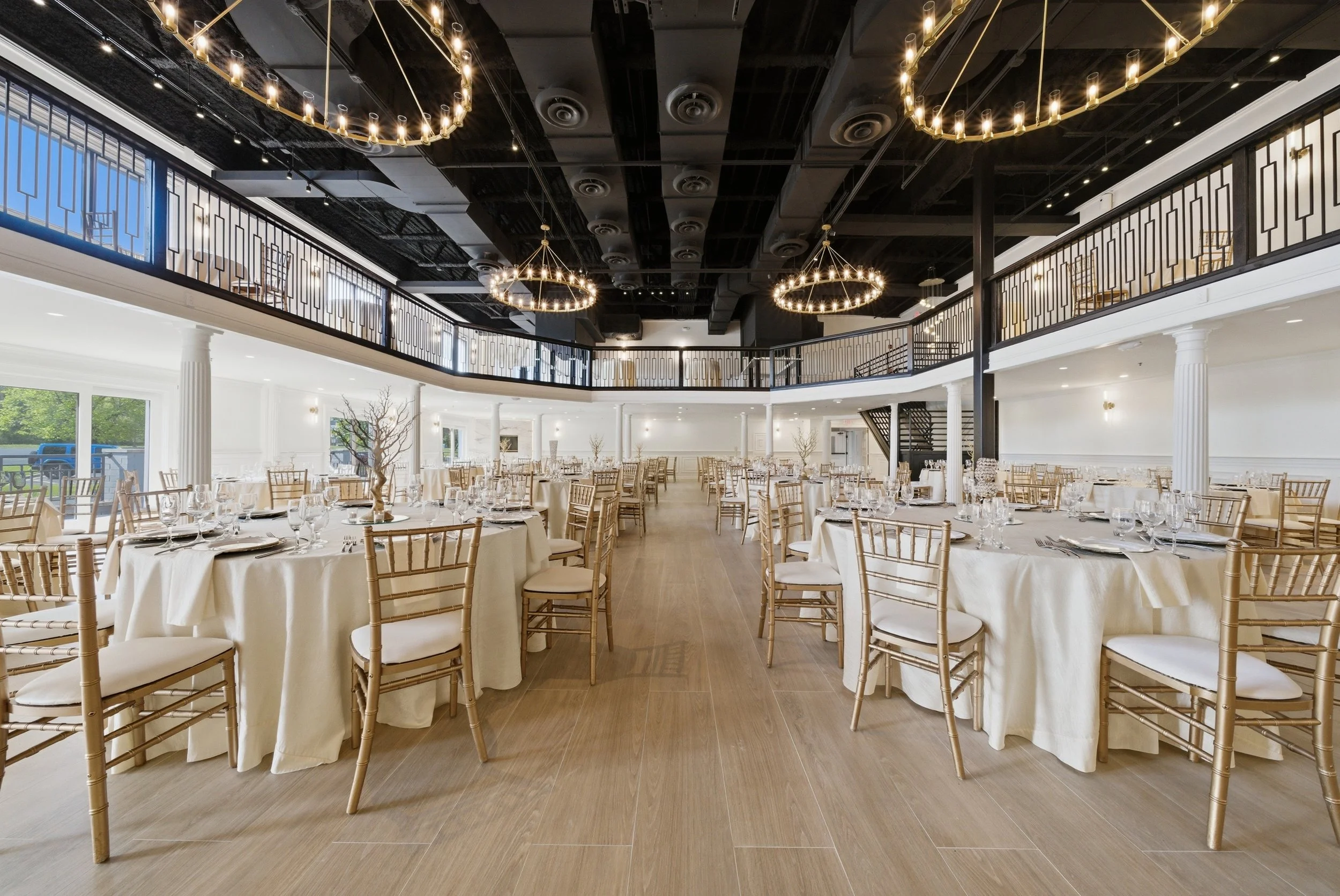 Elegant banquet hall decorated for a formal event with round tables, white tablecloths, gold chairs, and chandelier lighting.