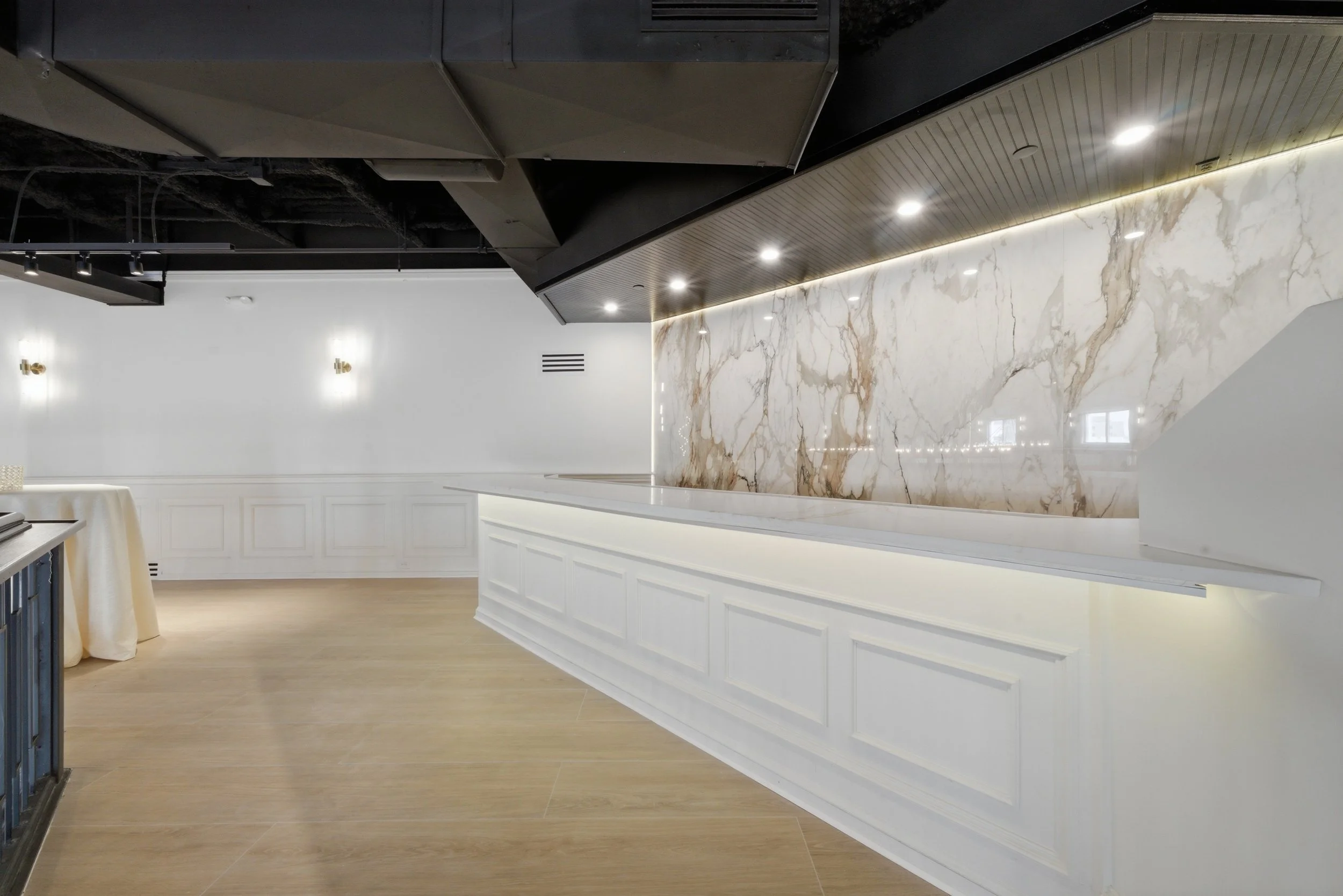 Interior view of a modern space with a white paneled counter, a marble wall, and a ceiling with black and wood accents and recessed lighting.