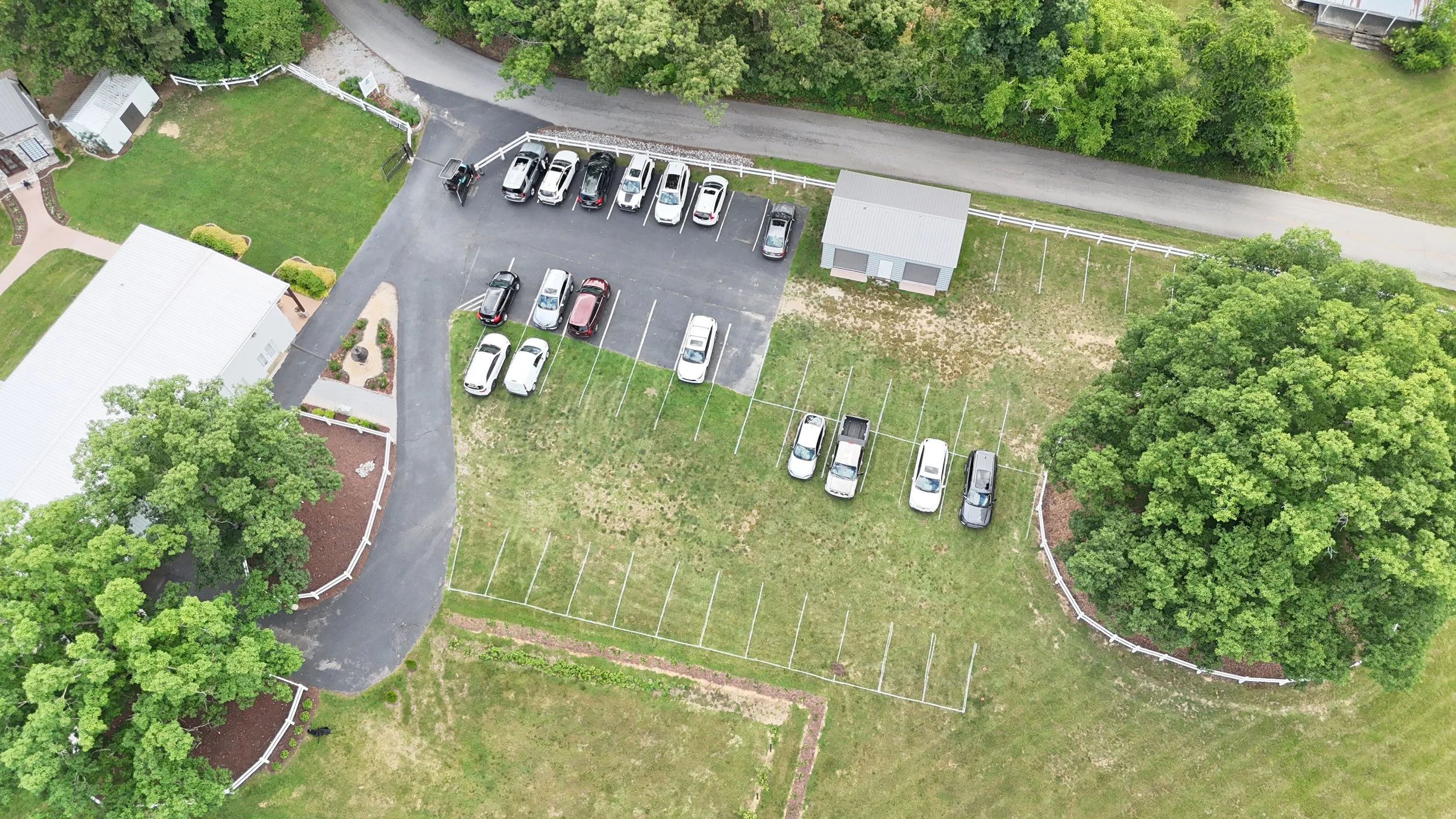 An aerial view of a large parking lot with cars, surrounded by greenery and trees.