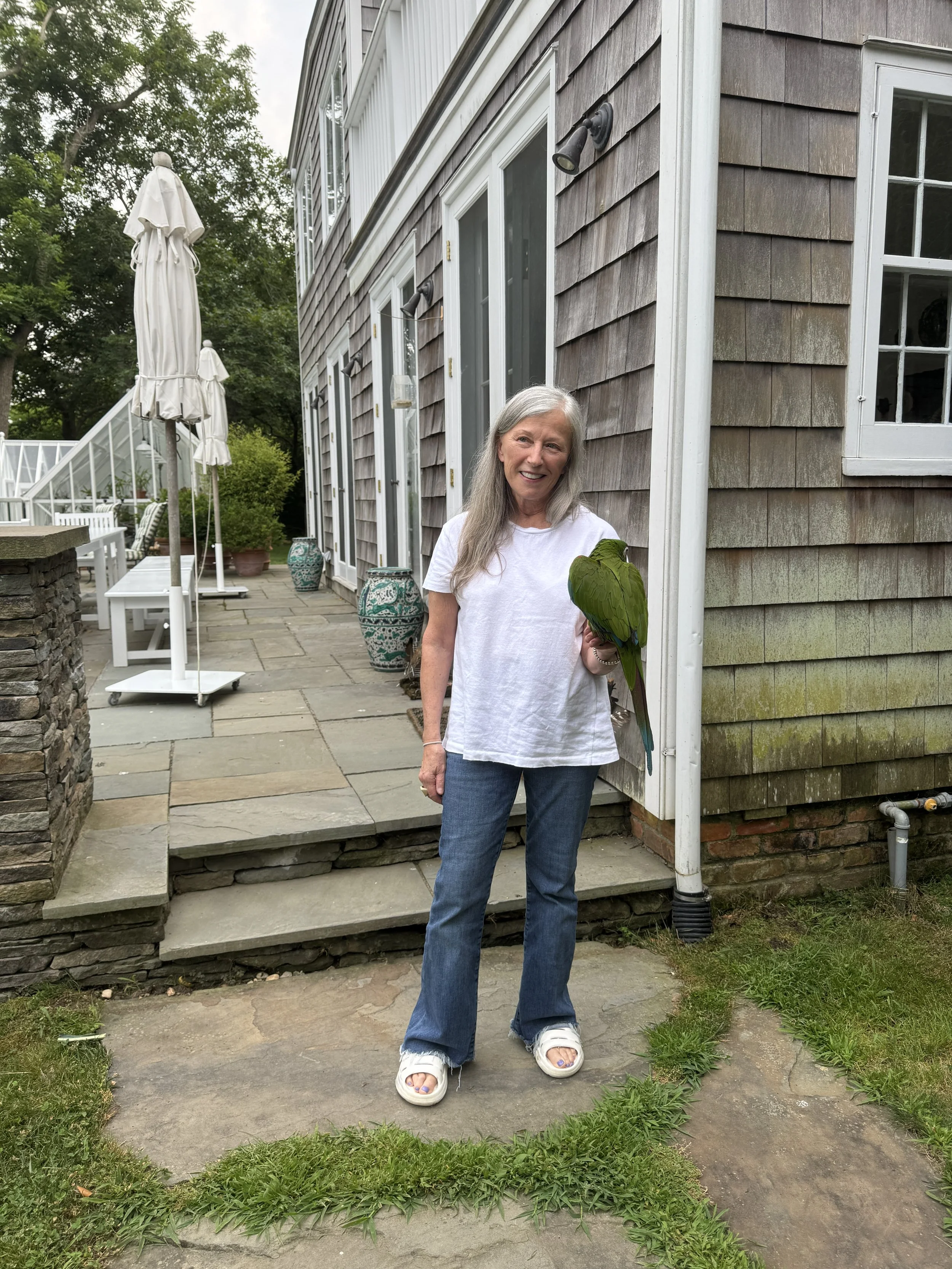 Cindy Sherman with a green parrot in her hand in front of an outside patio