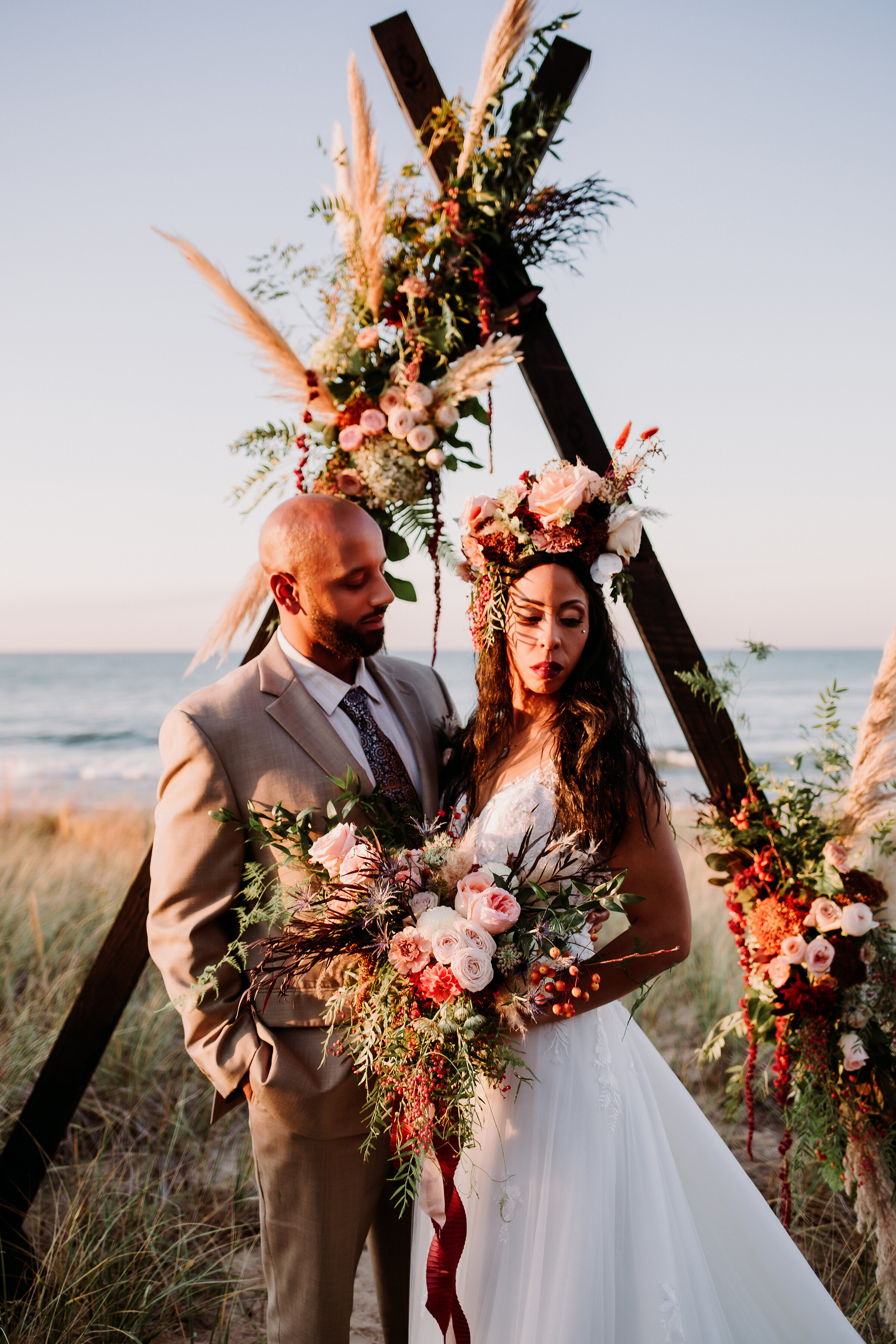  Elegant bohemian bride and groom modeling a vintage-inspired gown and handcrafted bouquet on the blue-sky shores of Lake Michigan at Indiana Dunes State Park. Boho florals beach elopement bride vintage wedding dress groom tan suit boho wedding arch 