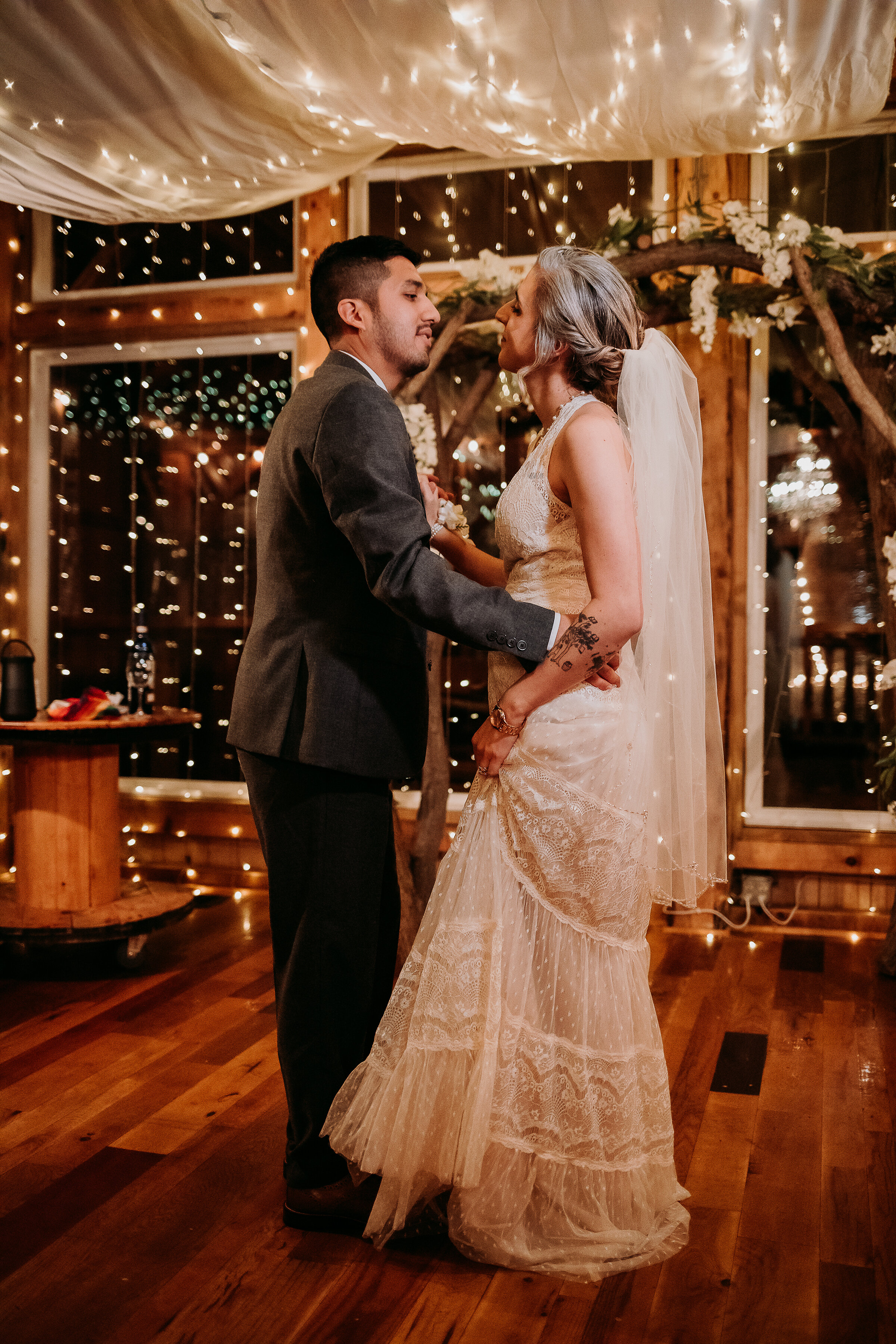  Kindred + Co. Photography captures romantic first dance moments under string lights, organza wedding decor, and floral wedding arch at this treehouse elopement. bohemian lace wedding dress, waist length wedding veil, gray tweed wedding suit, elopeme
