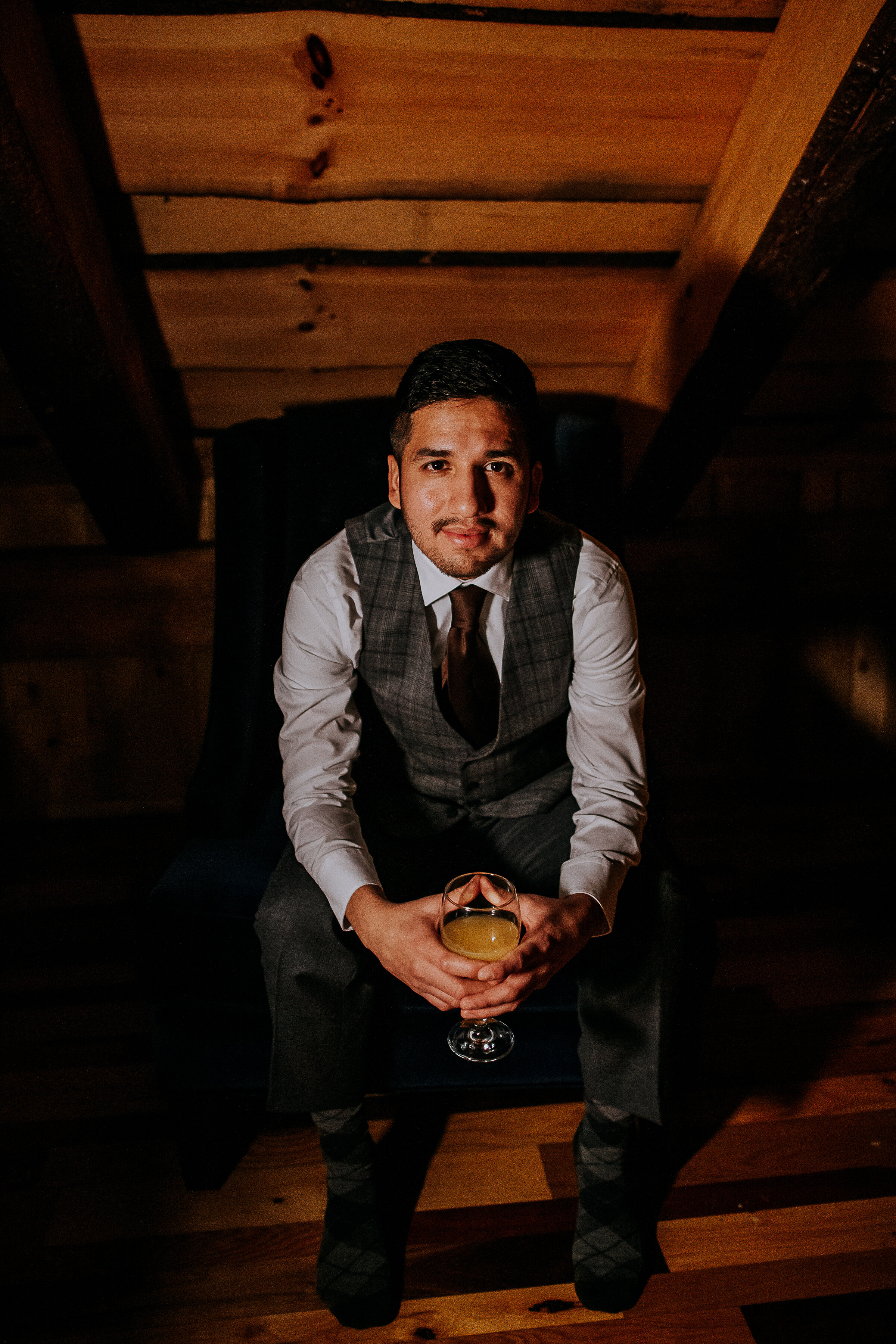  Kindred + Co. Photography captures groom eagerly awaiting his bride following a romantic candlelit elopement at the Grand Barn at the Mohicans. Gray tweed wedding best, wine colored wedding tie, groom, wedding wine, treehouse elopement, professional