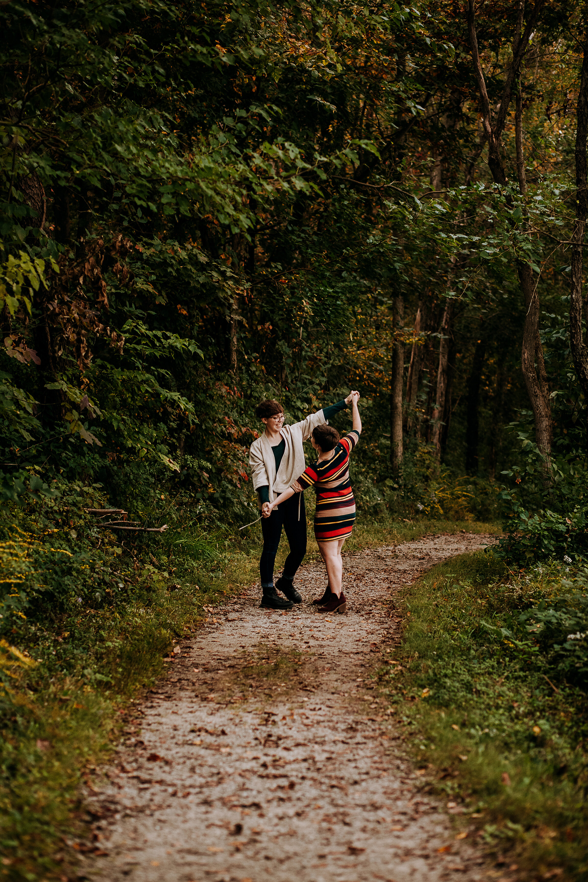  Beautiful candid shot of couple dancing outside on a trail covered in trees in this fall photo shoot in Indiana by Kindred + Co. photography. outdoor engagement photos candid engagement poses fall photoshoot fall outfit striped dress fort wayne indi
