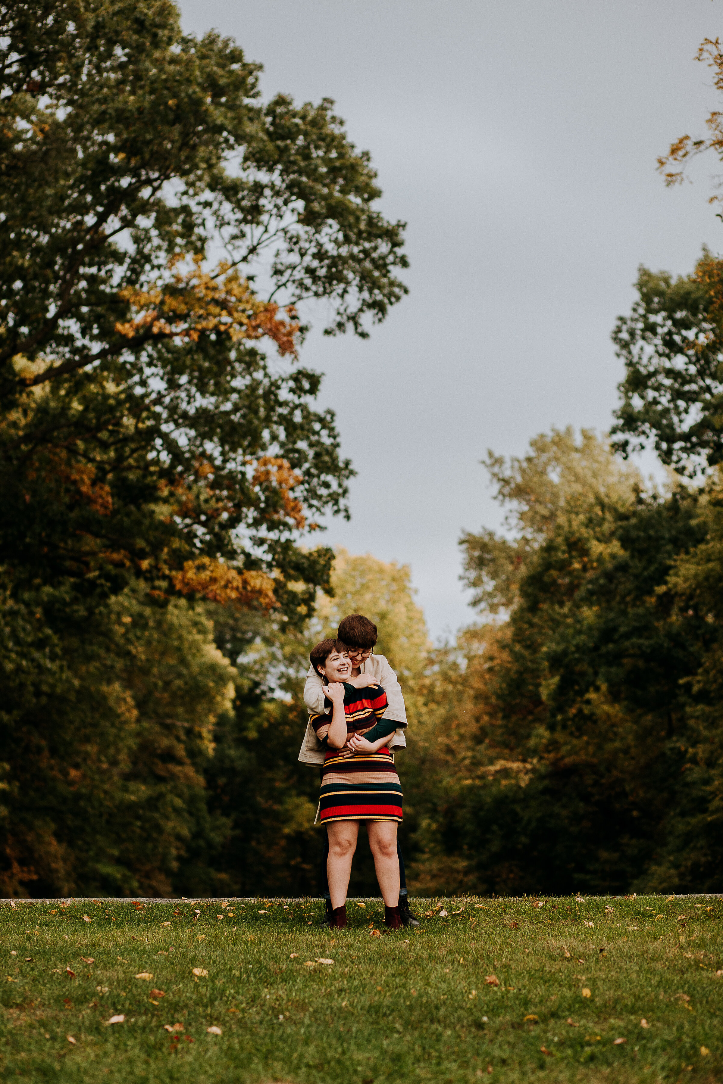  Cute couple holding each other in this outdoor fall photoshoot wearing a stripe fall color dress by Kindred + Co. photography in Indiana. bohemian photography fall photo shoot engagement photos same-sex couple poses fall outfit inspo how to style a 